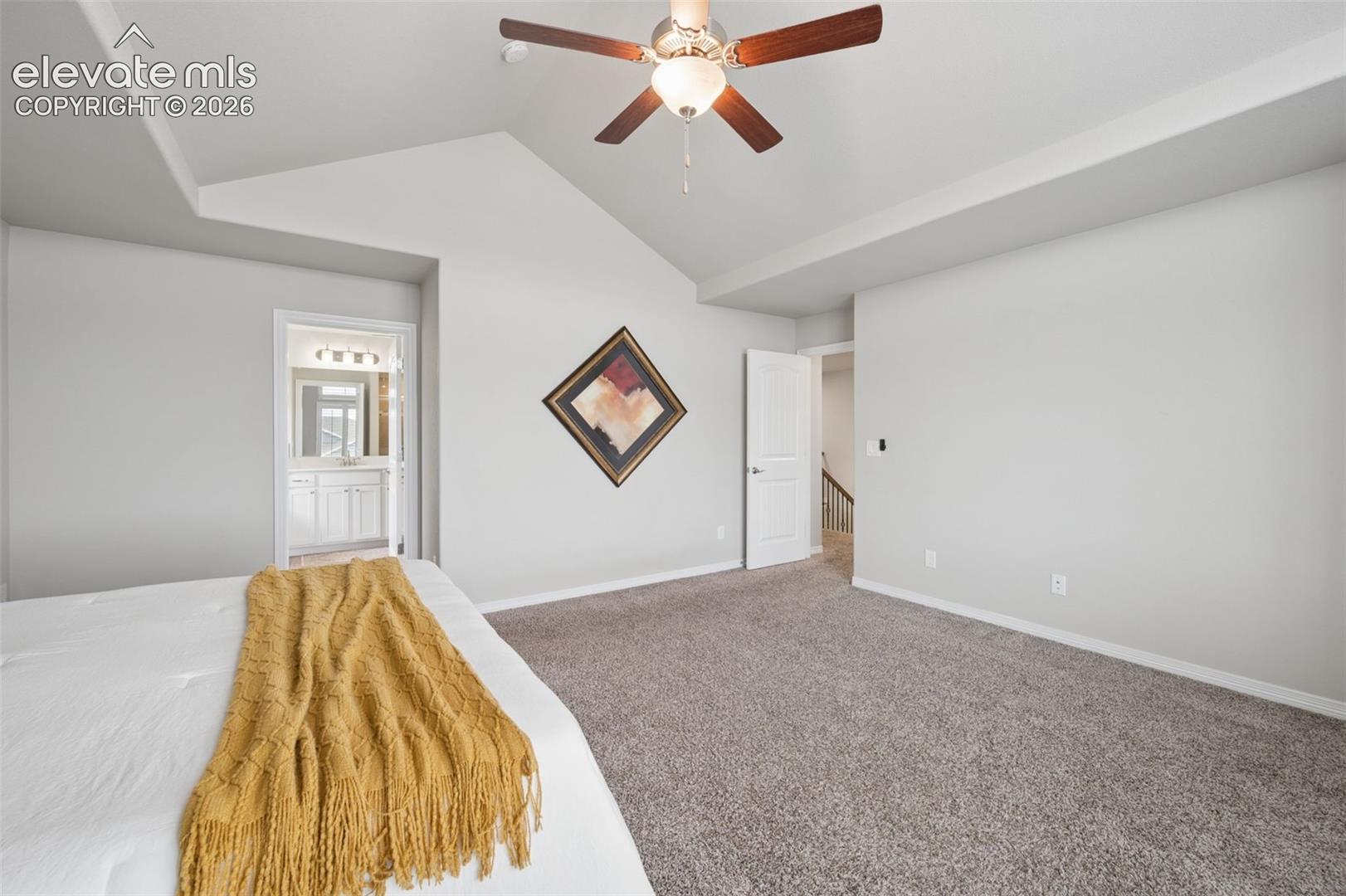 Vaulted ceiling with an attached ceiling fan, neutral wall paint, and gray carpet flooring