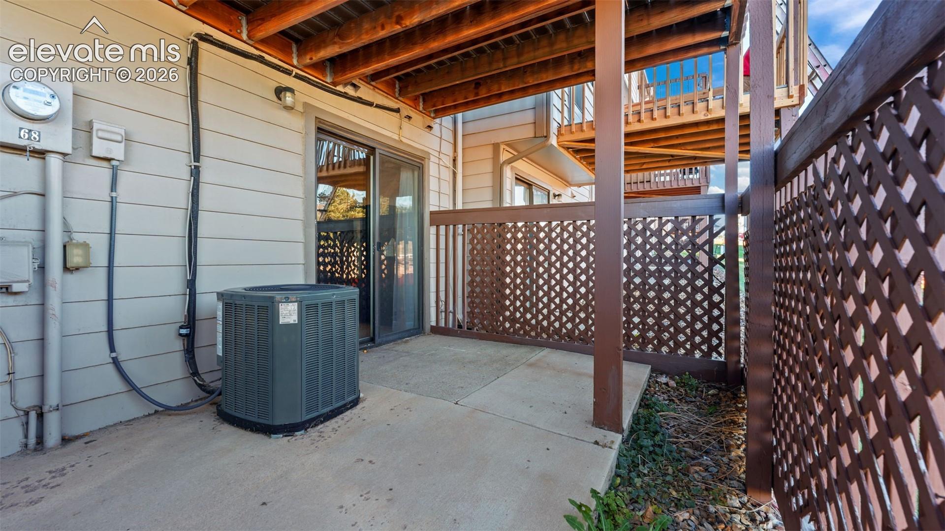 Concrete patio featuring a wood-lattice privacy screen, sliding glass door, and exposed structural wood ceiling joists