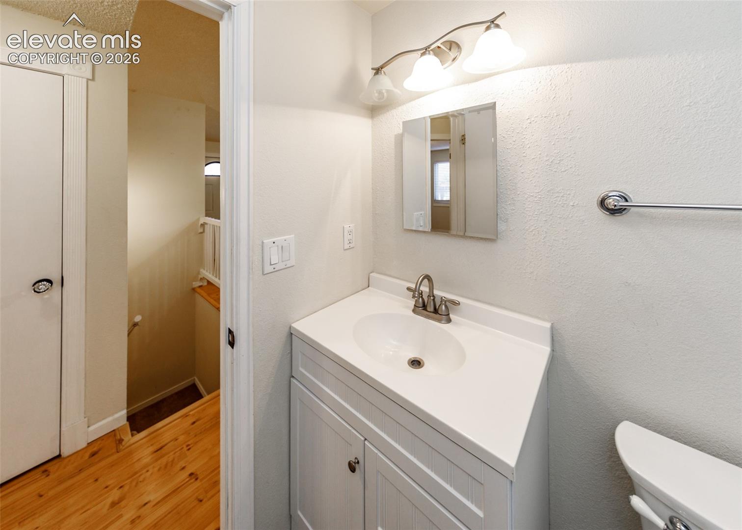 Single-sink vanity with white cabinet storage, integrated basin, polished metal faucet, wall-mounted three-light fixture, and recessed mirror