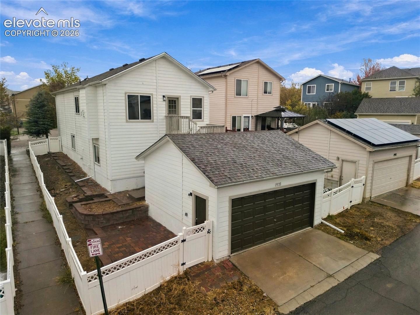 Two-story exterior featuring white vinyl siding, a detached single-car garage, fenced side yard, and paved patio area