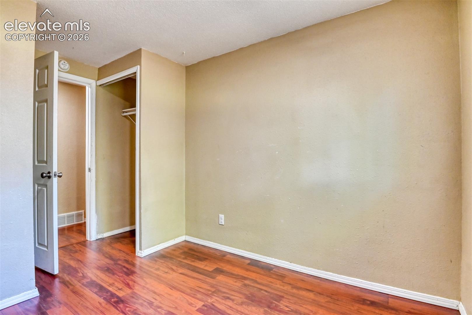 Interior room with wood-finish flooring, light tan wall color, white baseboards, and a white ceiling
