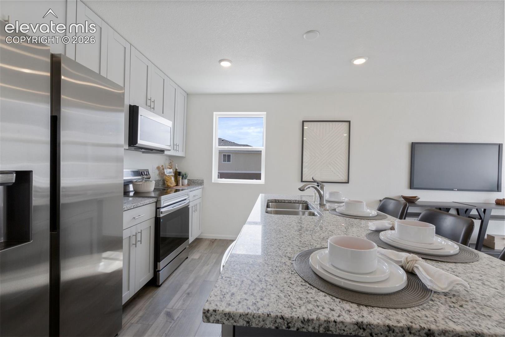 Kitchen featuring an island with granite countertops, stainless steel sink, wood-finish flooring, and recessed lighting
*photos of a model home*