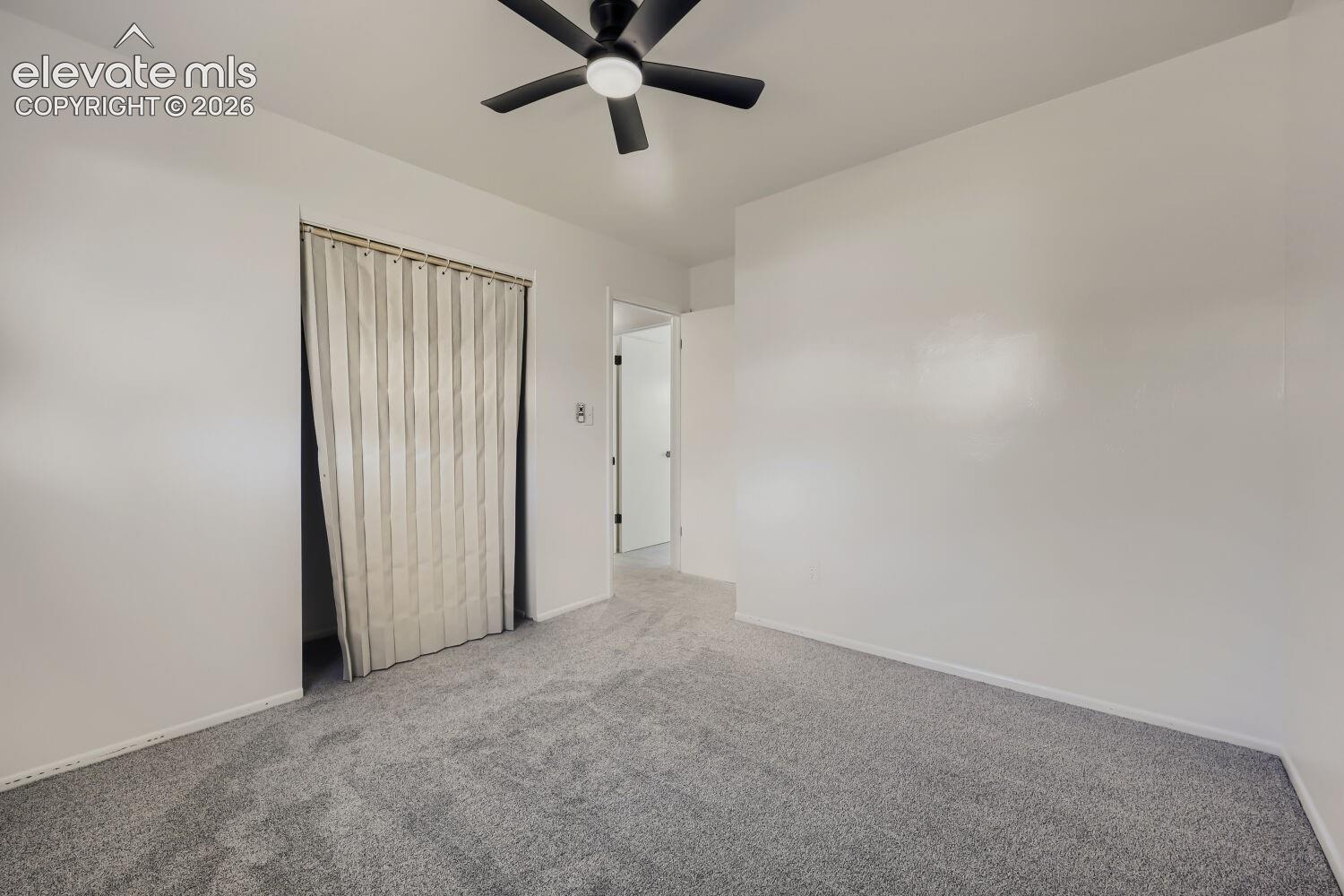 Plush grey carpeting, white painted walls, and a black ceiling fan with integrated lighting