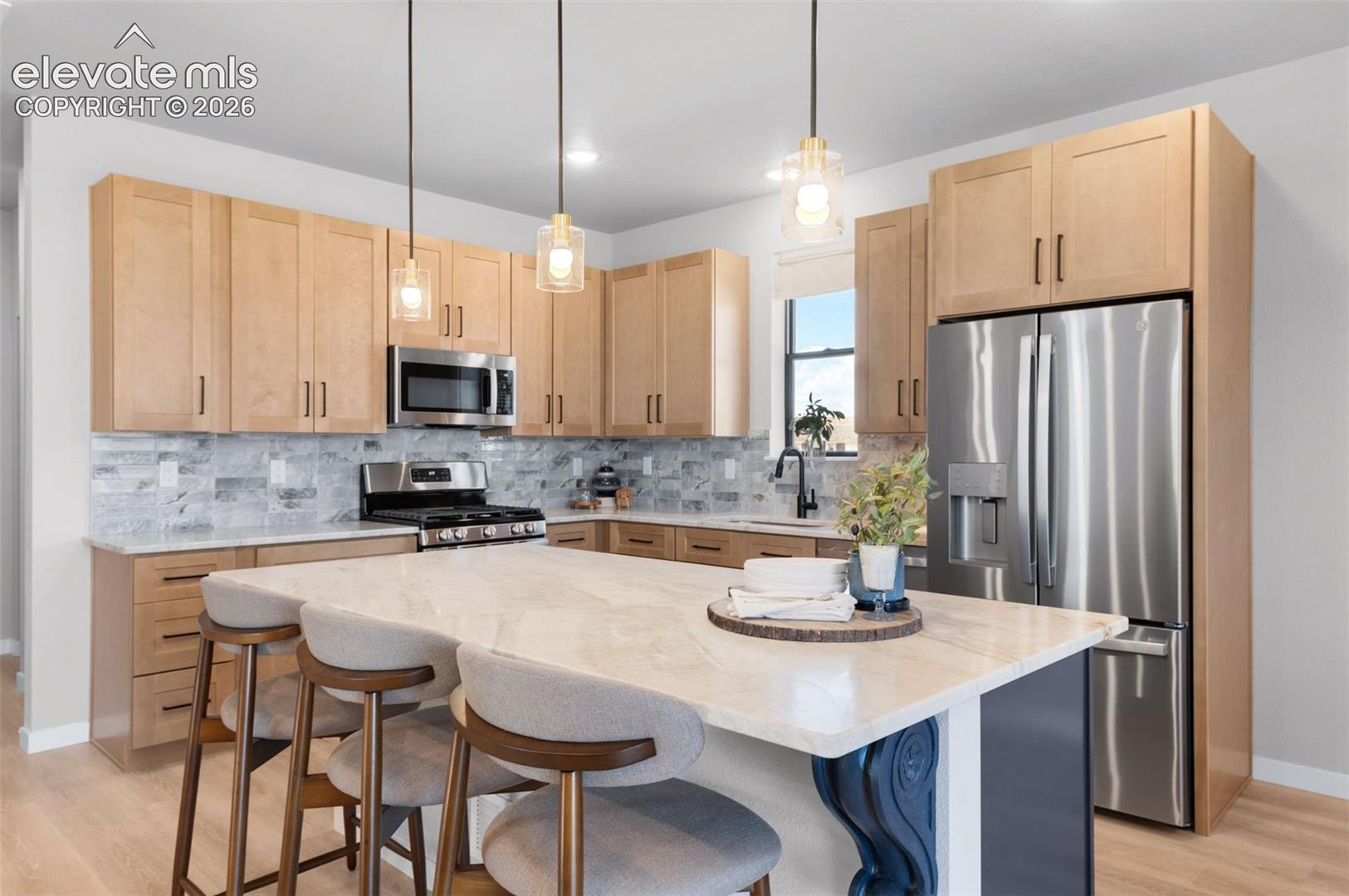 Kitchen featuring a central island with a light-toned countertop, stainless steel appliances, light wood-finish cabinetry, tile backsplash, and light wood-finish flooring