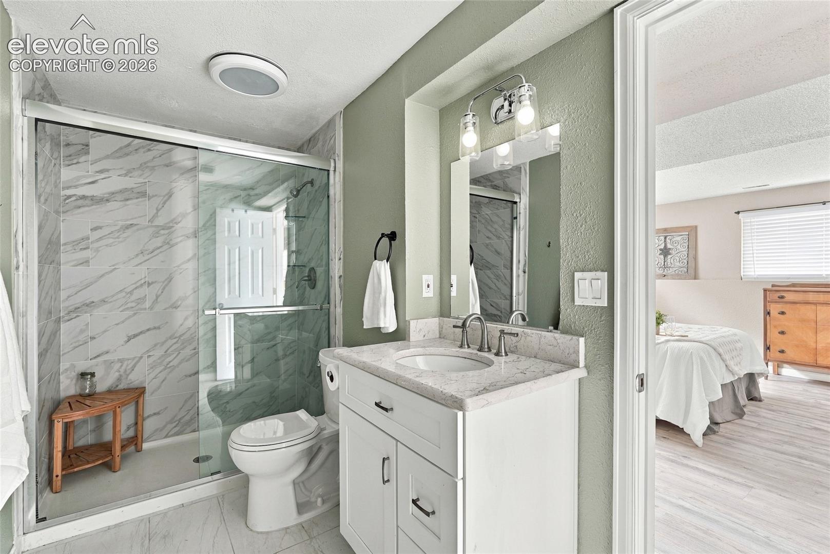 Bathroom featuring a glass-enclosed shower with tiled walls, a vanity with a white countertop and basin sink, and wood-finish flooring