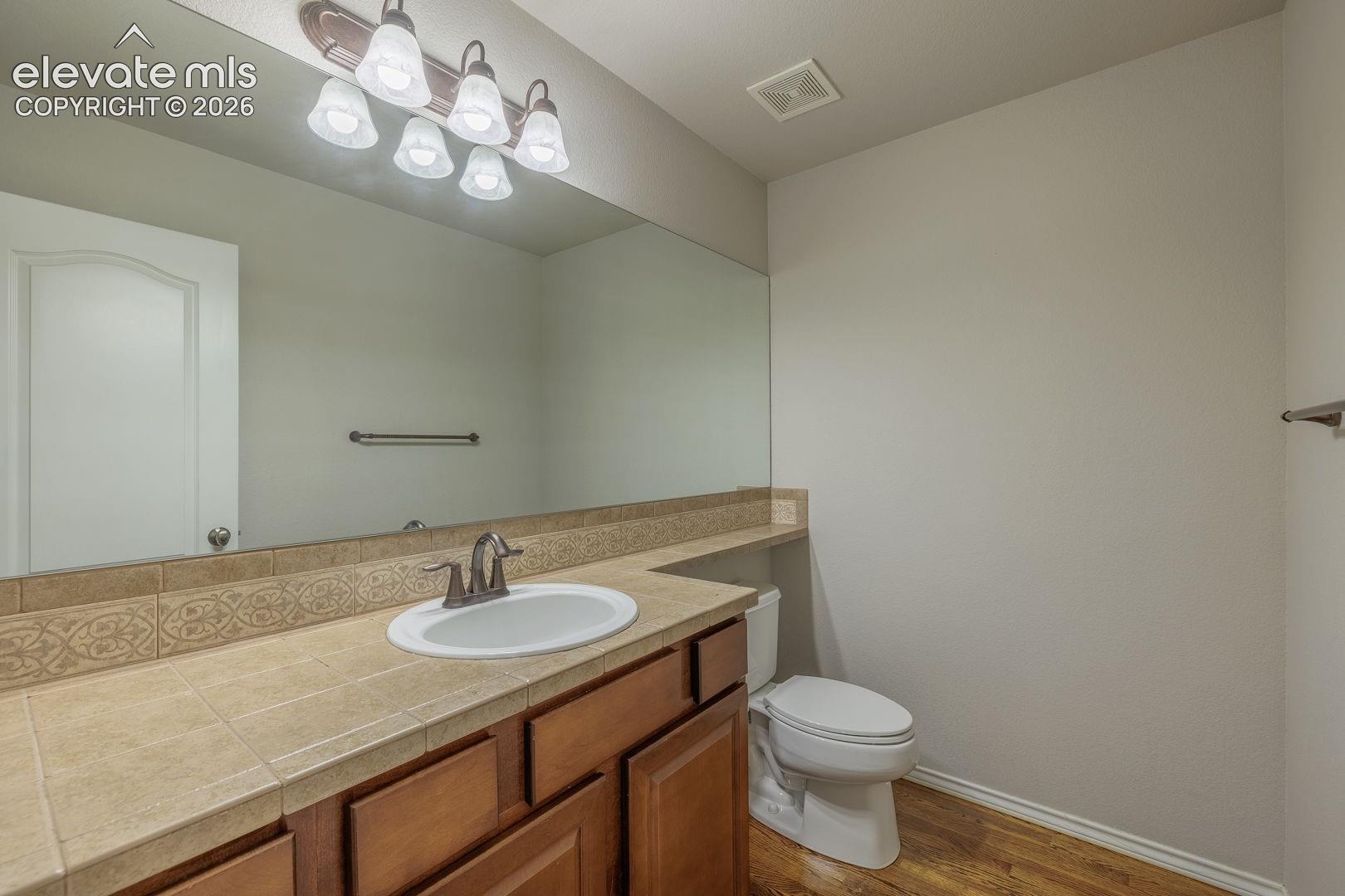 Spacious bathroom featuring a wood-finish vanity with dual-sink basin, ceramic countertop, and chrome faucet fixtures