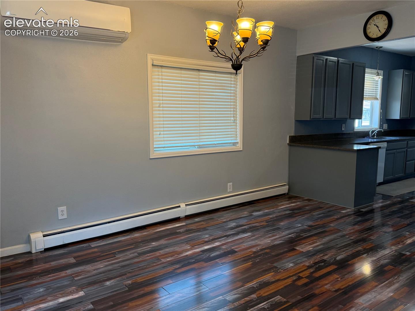 Wood-finish flooring, wall-mounted ductless climate control unit, iron-style chandelier, and dark cabinetry with contrast countertops