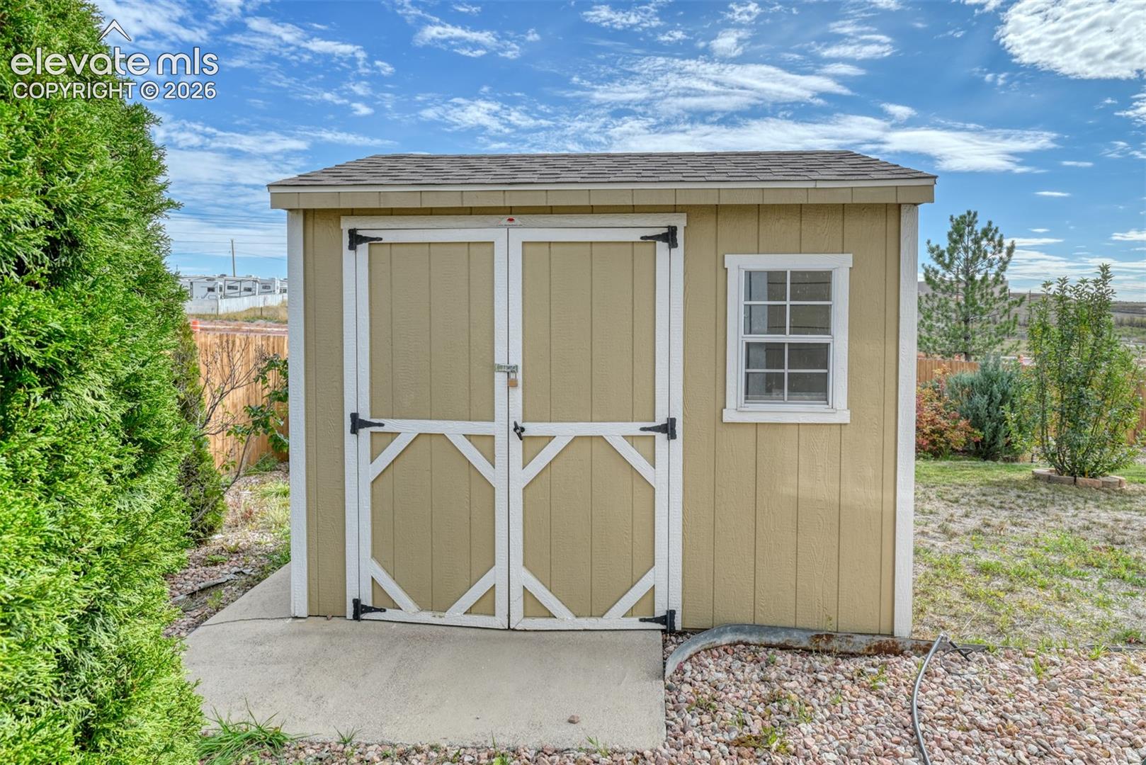 Detached storage shed featuring wood-composite siding, a shingled roof, double swing doors, and a single-pane window