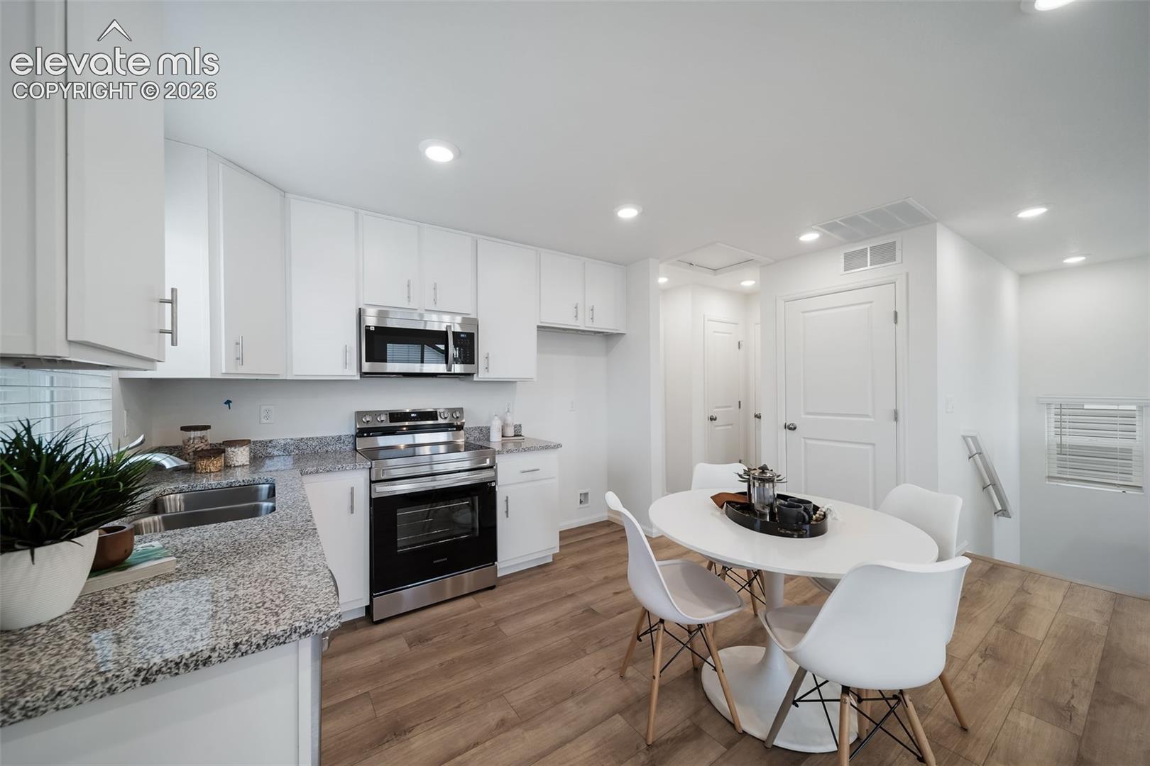 Kitchen featuring white cabinetry, stainless steel appliances, granite countertops, and wood-finish flooring
*photos of a model home*