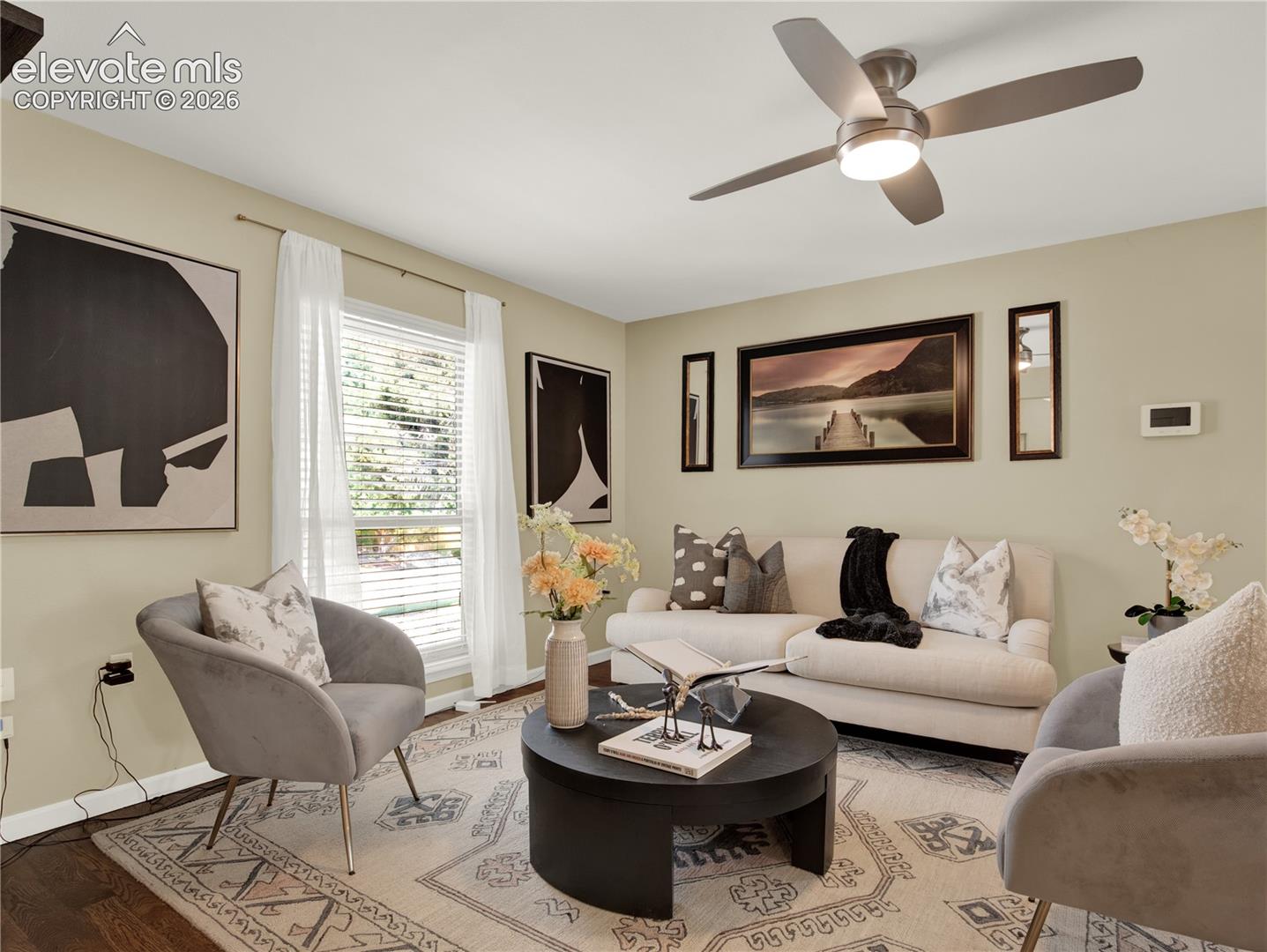 Living area featuring dark wood-finish flooring, a contemporary ceiling fan with integrated lighting, and a window with horizontal blinds