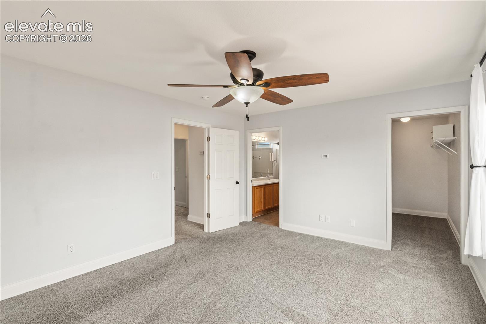 Interior featuring neutral carpeting, a ceiling fan with integrated lighting, multiple doorways, a walk-in closet with built-in shelving, and an attached bathroom featuring wooden cabinetry