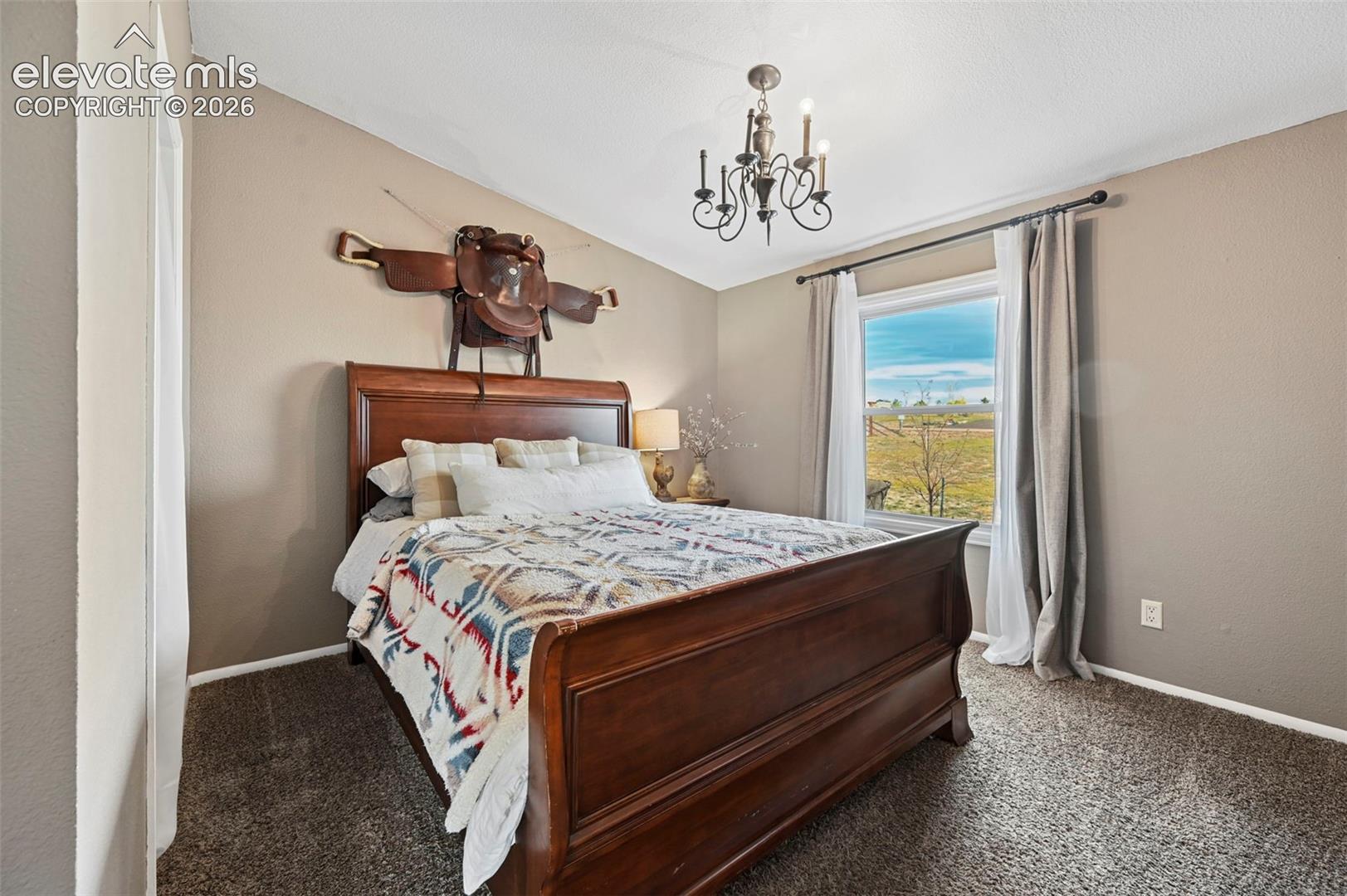Room featuring textured wall-to-wall carpeting, neutral wall paint, a wrought-iron style chandelier, and a window with exterior landscape exposure