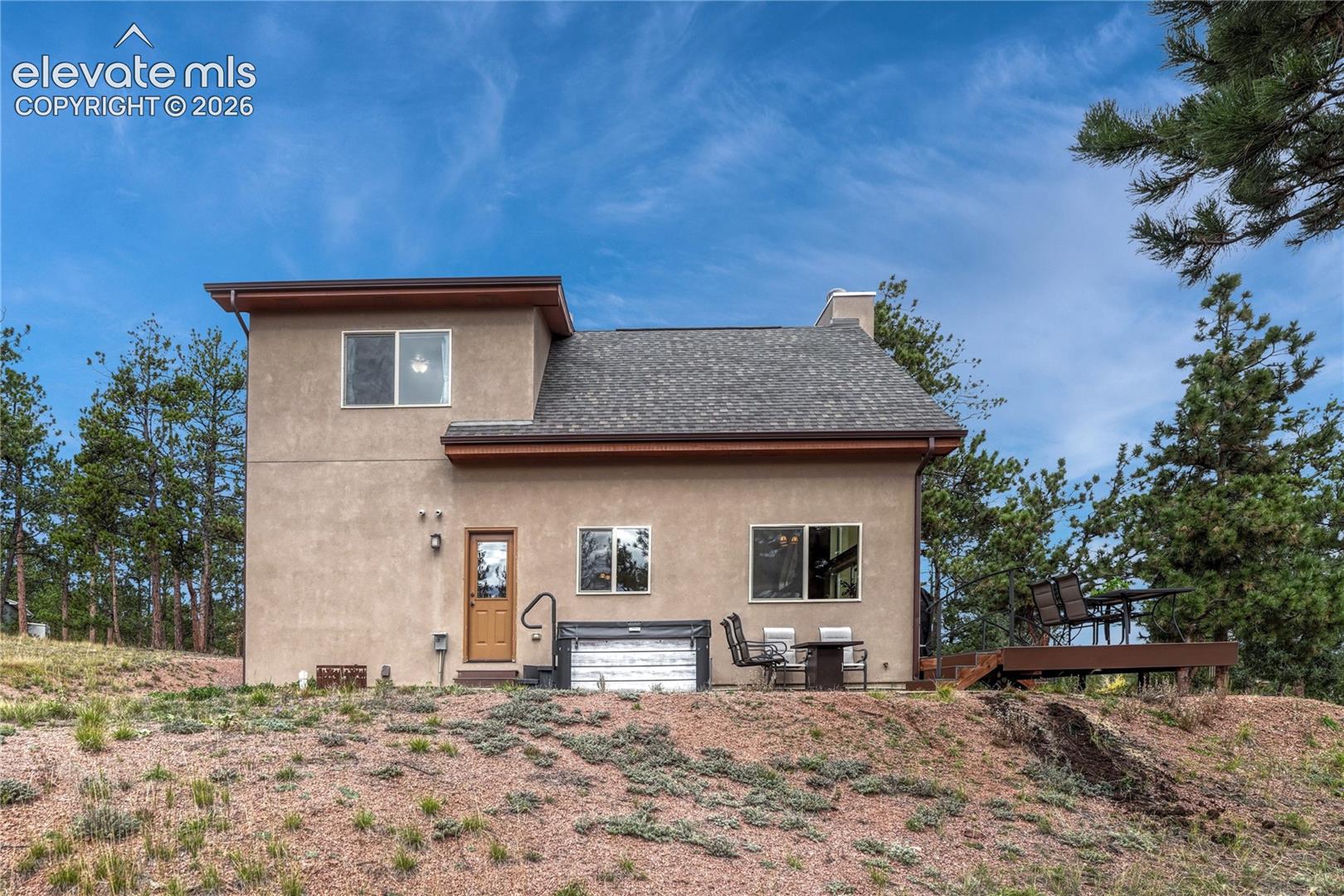 residence featuring stucco siding, a multi-pitched roof, an elevated wooden deck, and an installed exterior hot tub