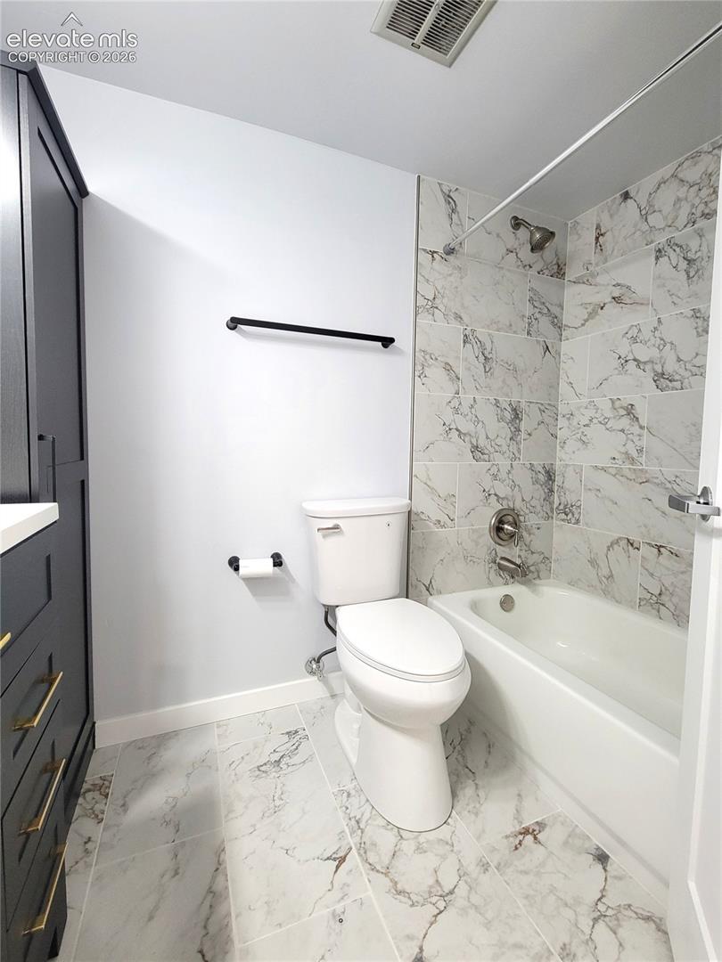 Bathroom featuring a white bathtub with a shower, a modern toilet, and an elegant vanity with brass hardware