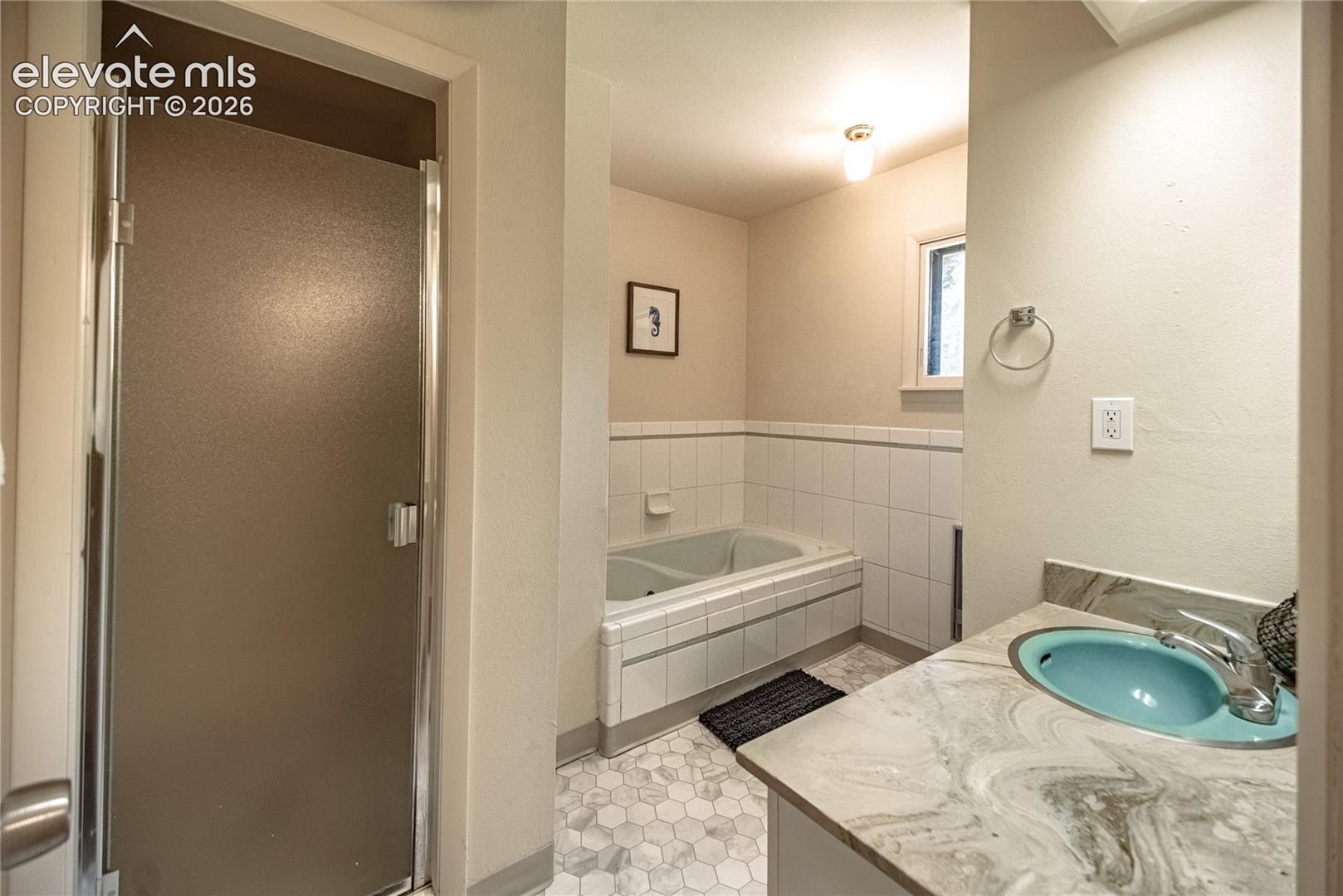 Frosted glass shower enclosure, built-in bathtub, vanity with integrated sink, patterned countertop, and hexagonal floor tiling