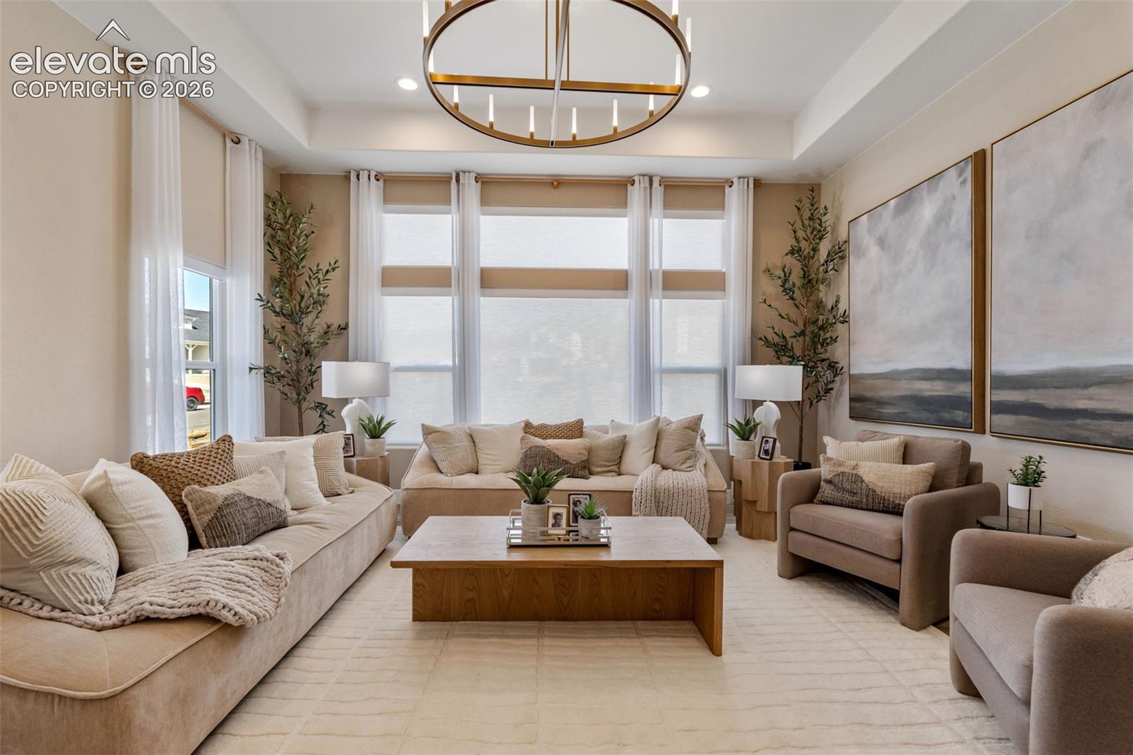 Tray ceiling featuring a contemporary circular chandelier and extensive windows with integrated window treatments