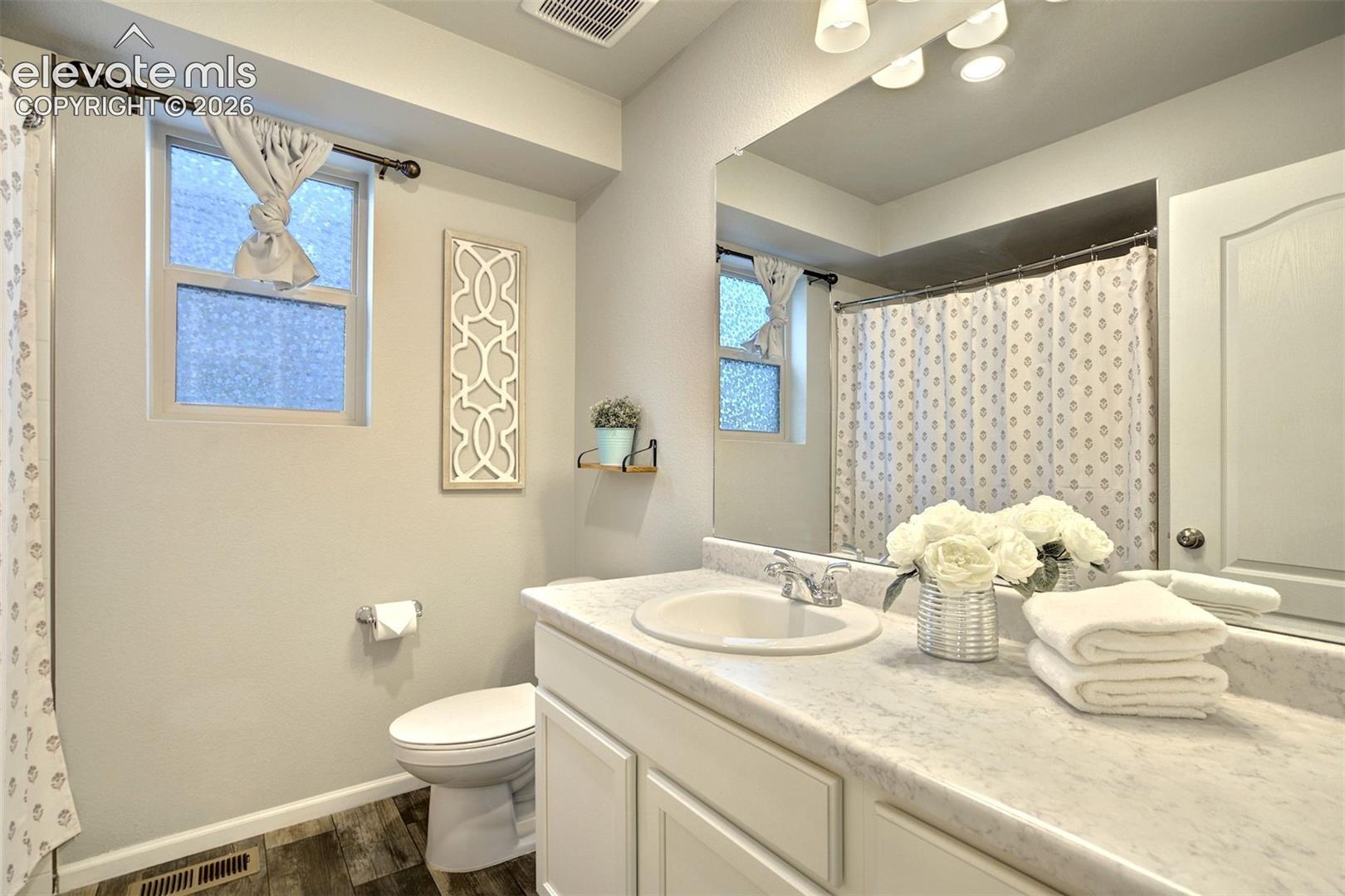 Bathroom featuring a vanity with a stone-finish countertop, integrated sink, large wall-mounted mirror, and wood-finish flooring