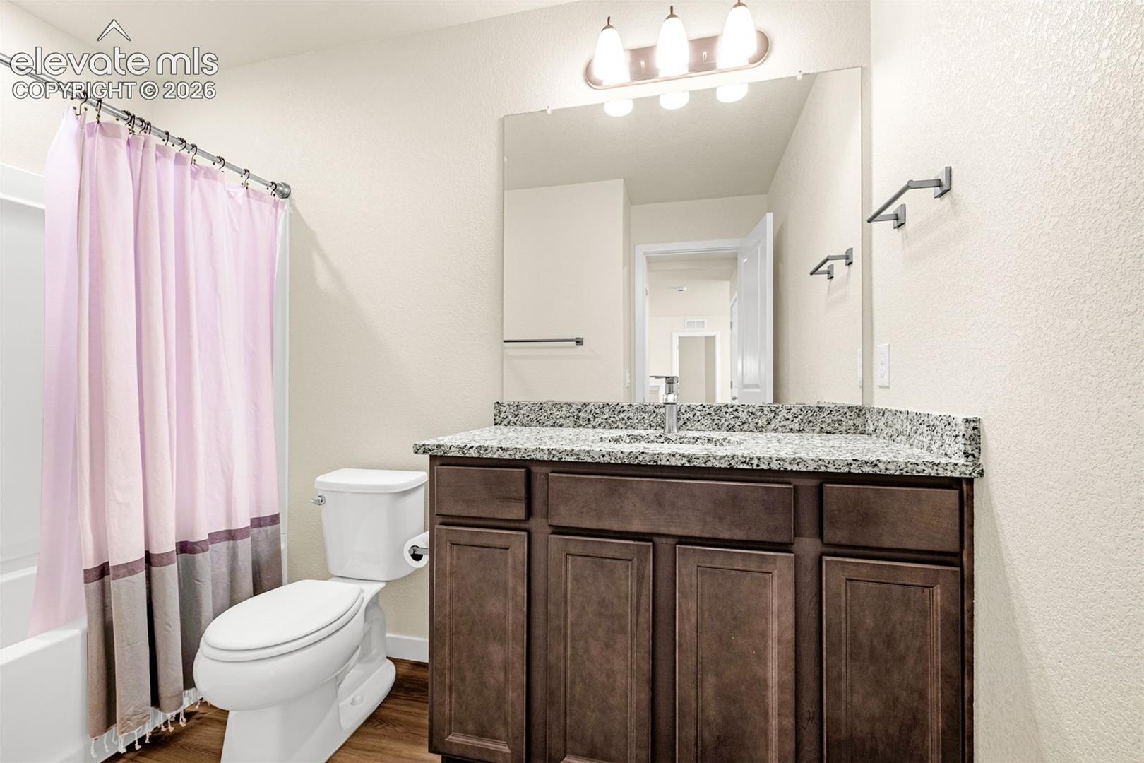 Bathroom featuring a vanity with a stone countertop, dark wood-finish cabinetry, an integrated sink, and an overhead light fixture