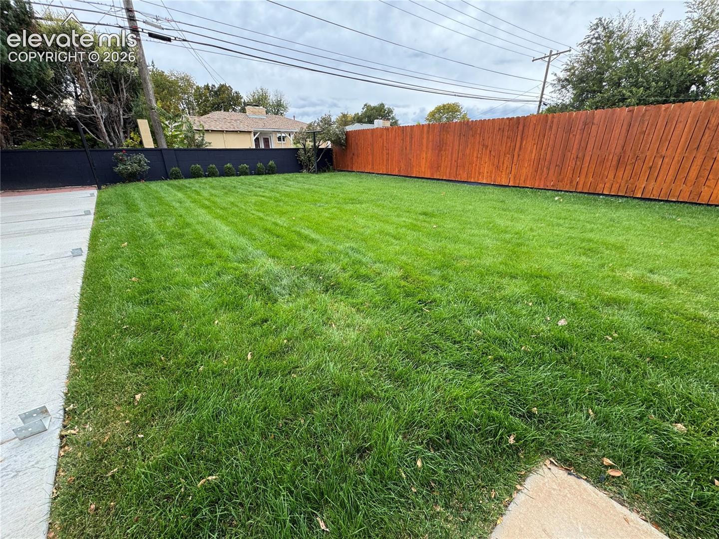 Expansive backyard featuring a level lawn, concrete patio border, wood-stain privacy fencing, and dark-finished perimeter fencing