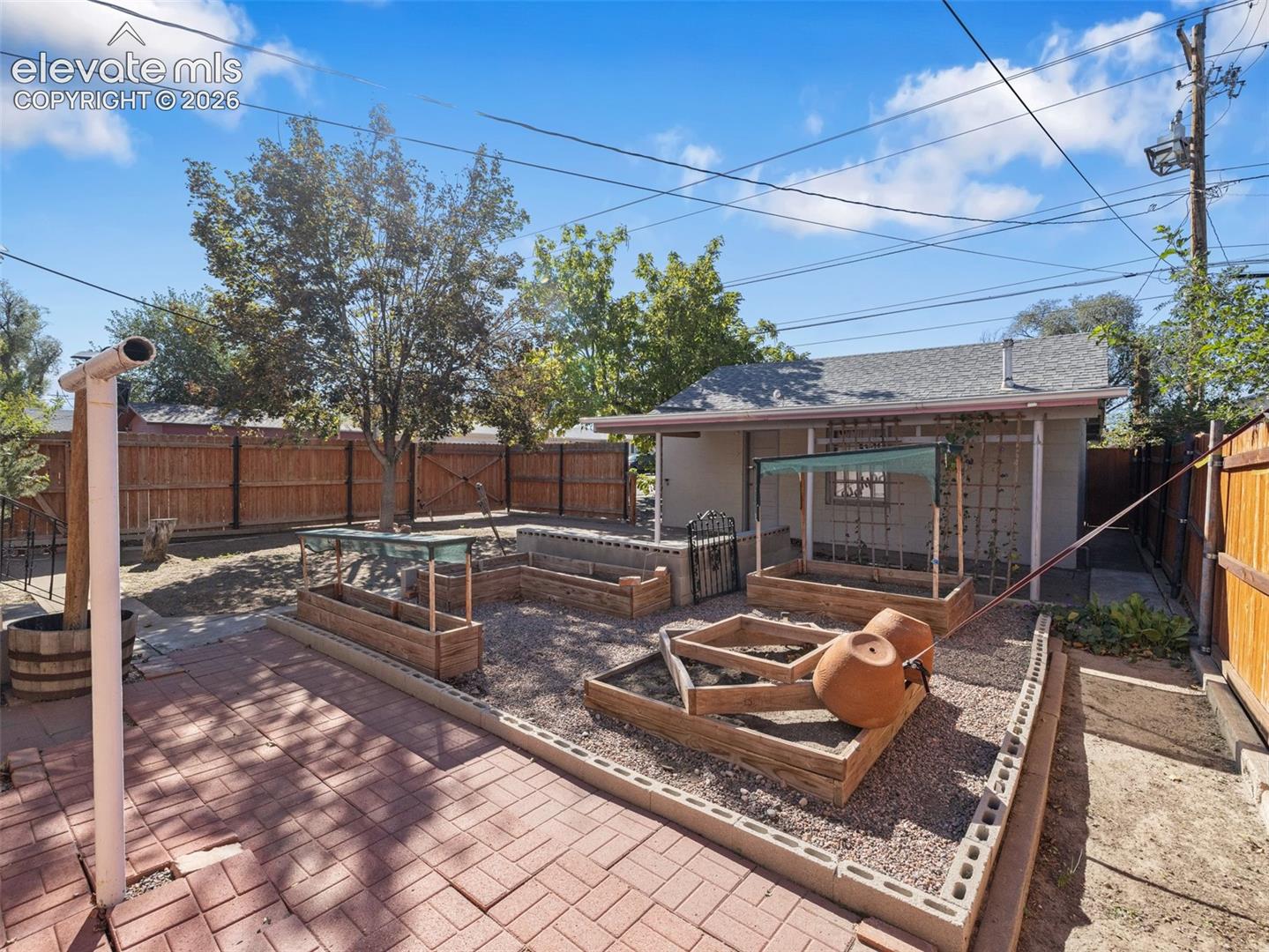 Outdoor space featuring a paved brick patio, raised wooden garden beds, gravel ground cover, and full-height perimeter wood fencing