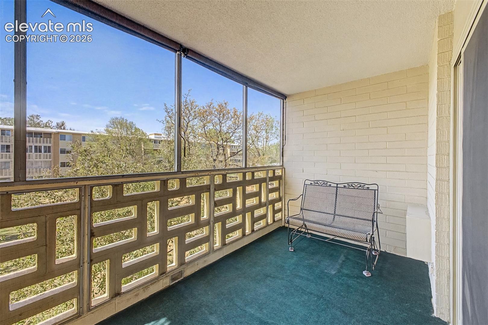Enclosed balcony featuring a patterned concrete screen wall, large windows, brick-finish wall, and green carpeting