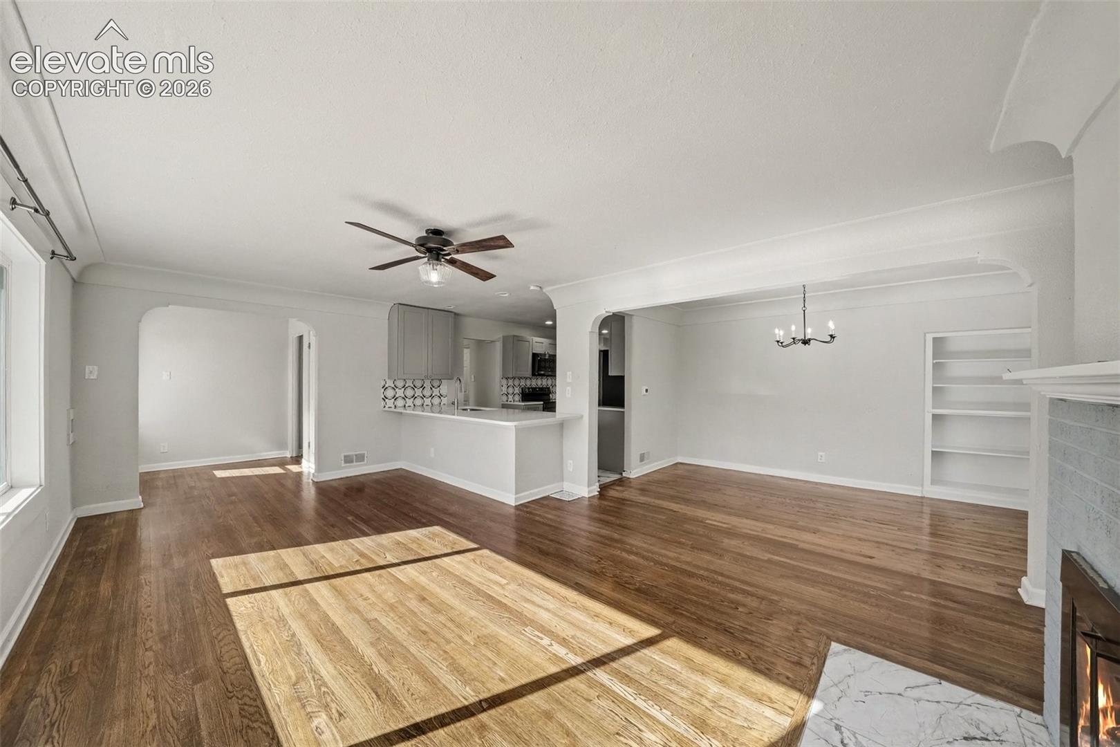 Open floor plan featuring wood-finish flooring, arched doorways, a stone-surround fireplace, and built-in shelving