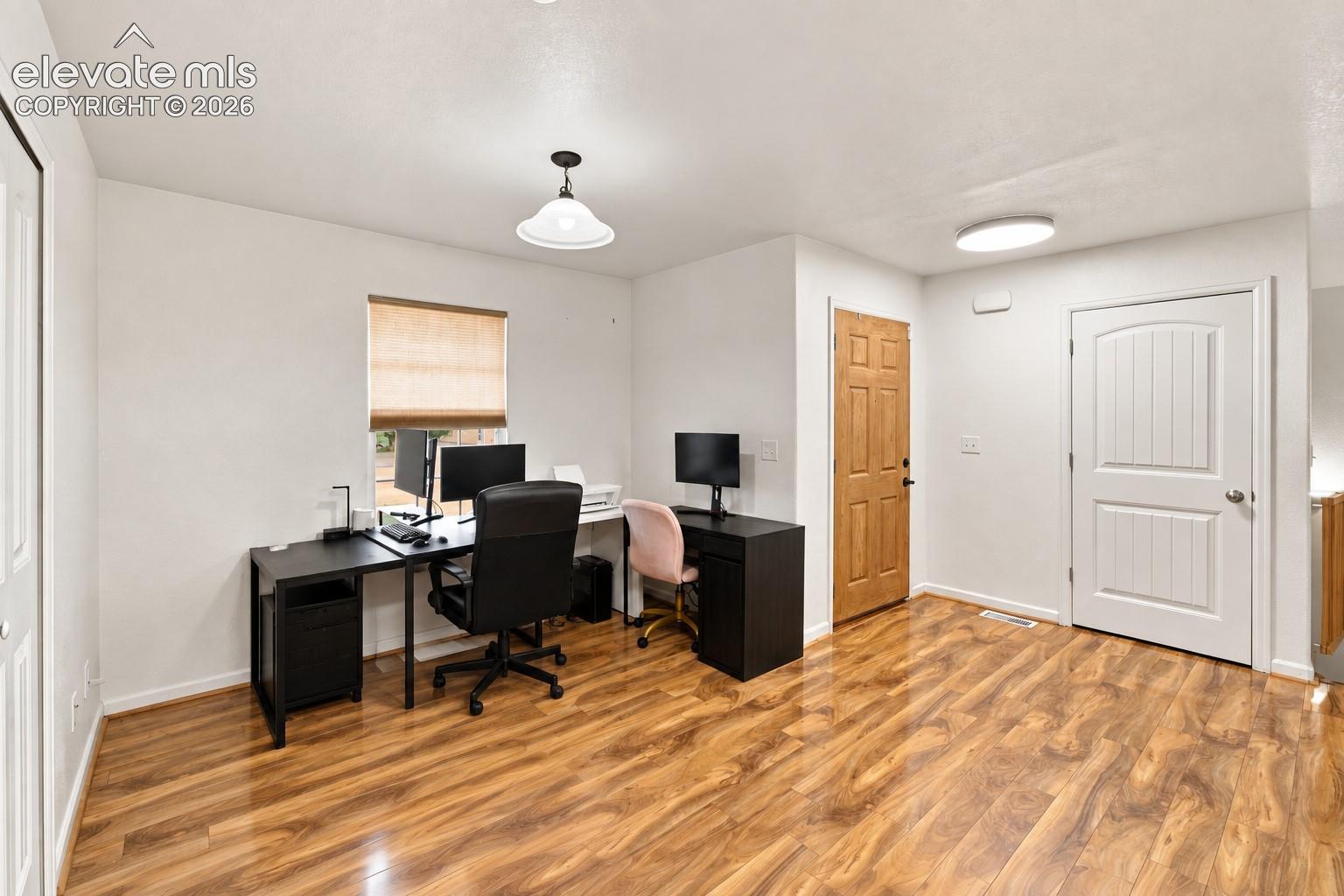 Wood-finish flooring, white paneled door, flush-mount ceiling lighting, and a single window with a blind