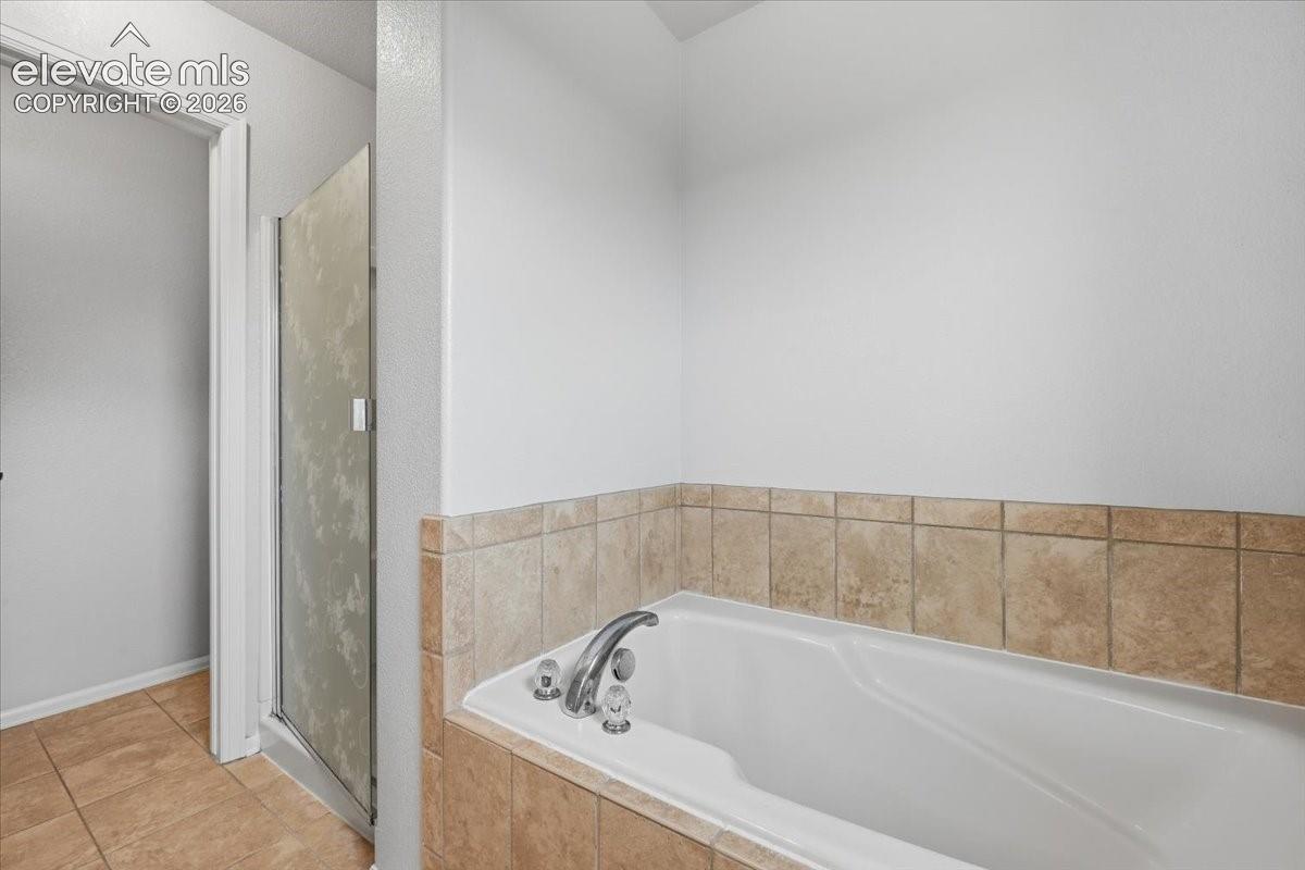 Built-in soaking tub with chrome fixtures, surrounded by tiled decking and wainscoting