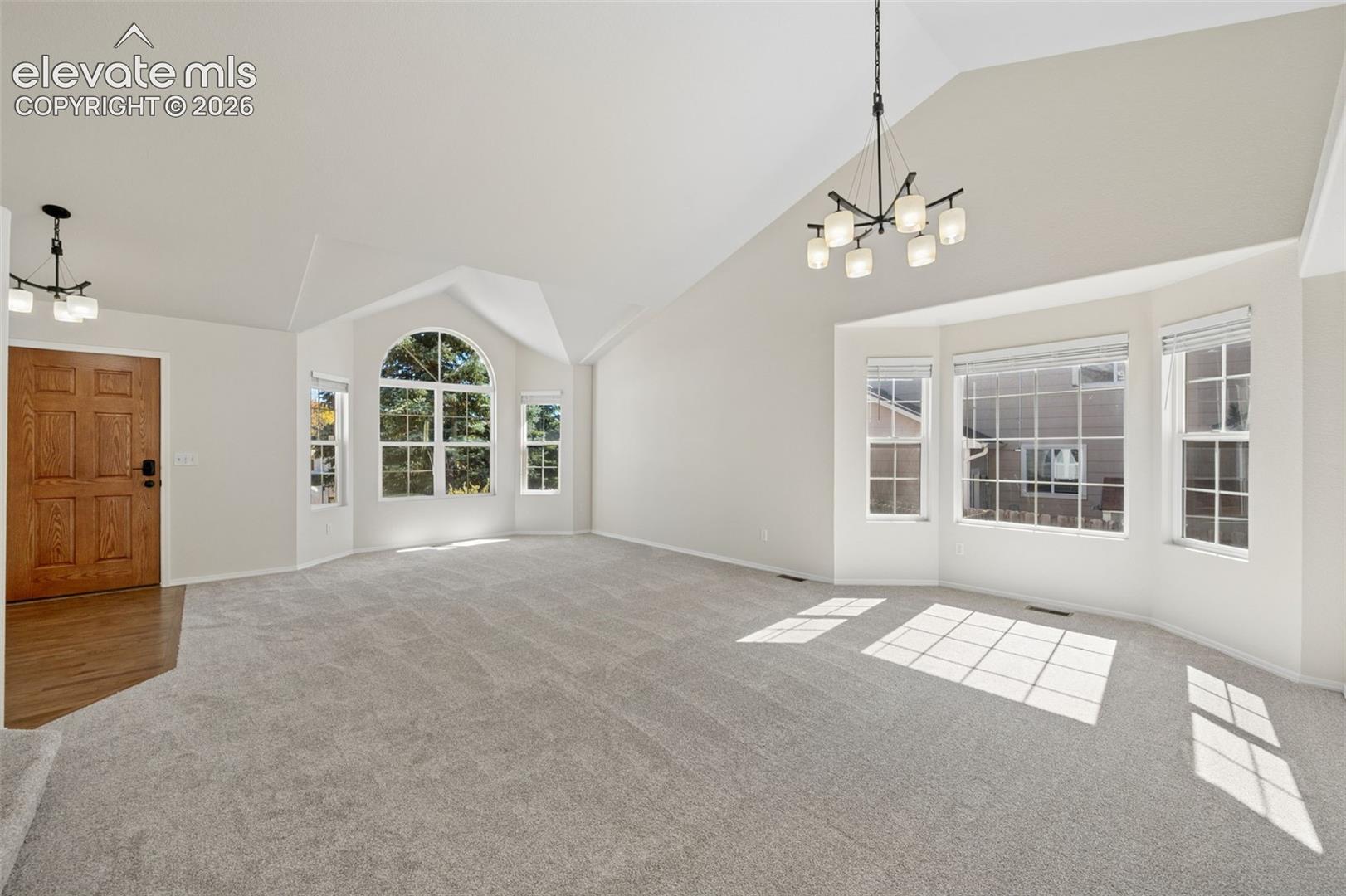 Vaulted ceilings featuring multi-tiered hanging light fixtures, expansive bay windows, and neutral carpeting