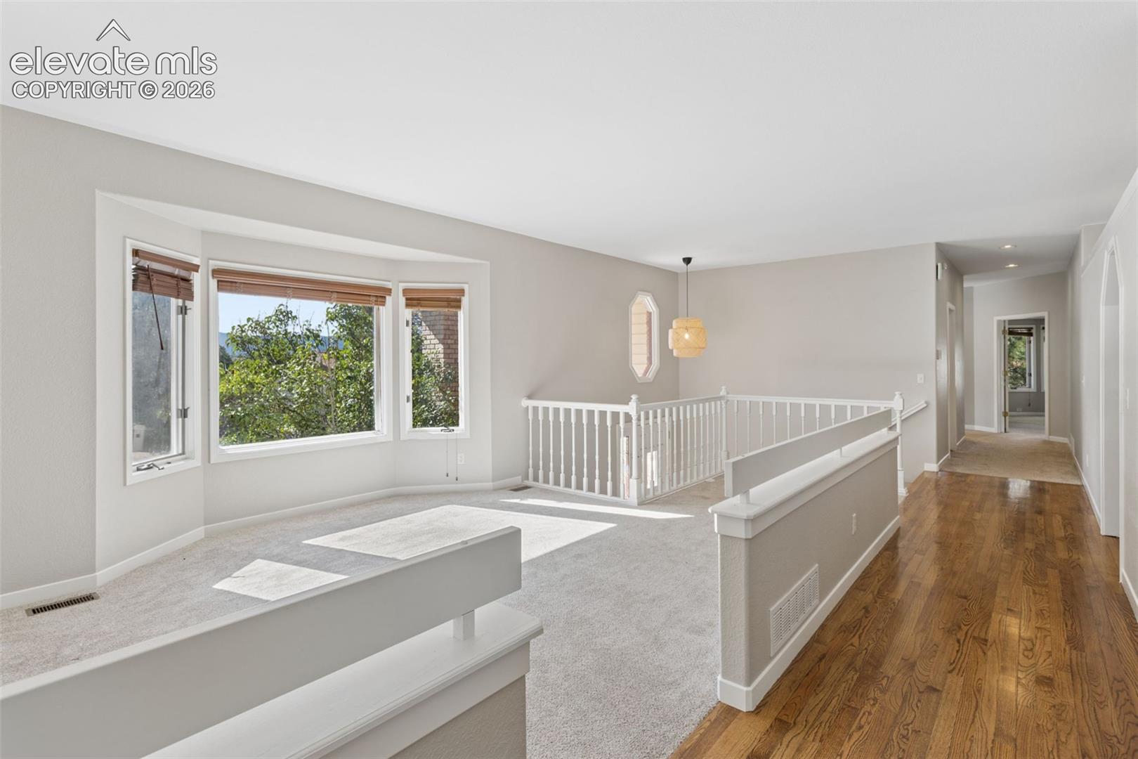 Bay window with natural light, wood-finish flooring, carpeted area, white banister, and a decorative light fixture
