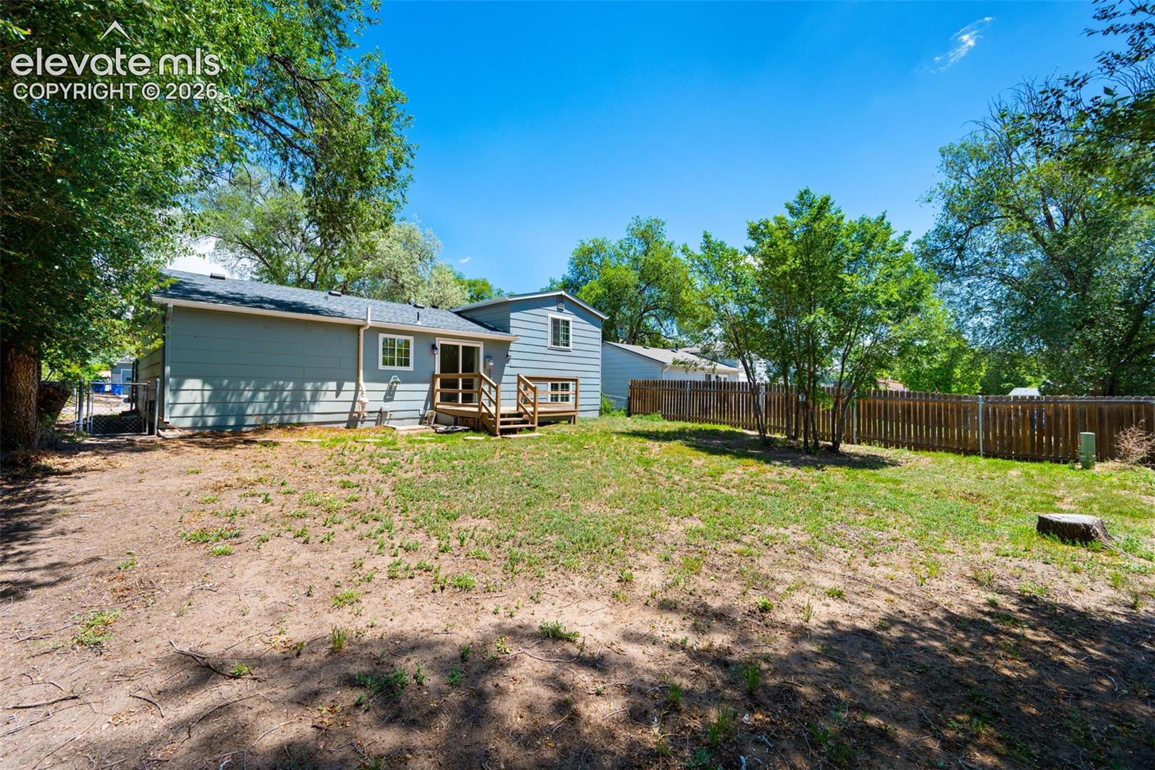 Expansive backyard with privacy fencing, mature trees, and a wooden deck