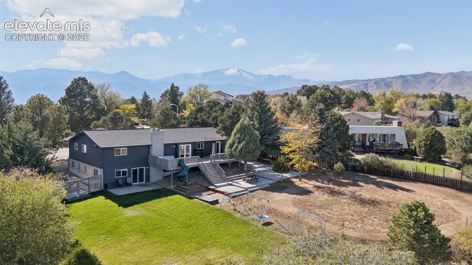 Exterior featuring vertical siding, elevated wooden deck, stone-finish chimney, multi-level hardscaping, and mountain backdrop