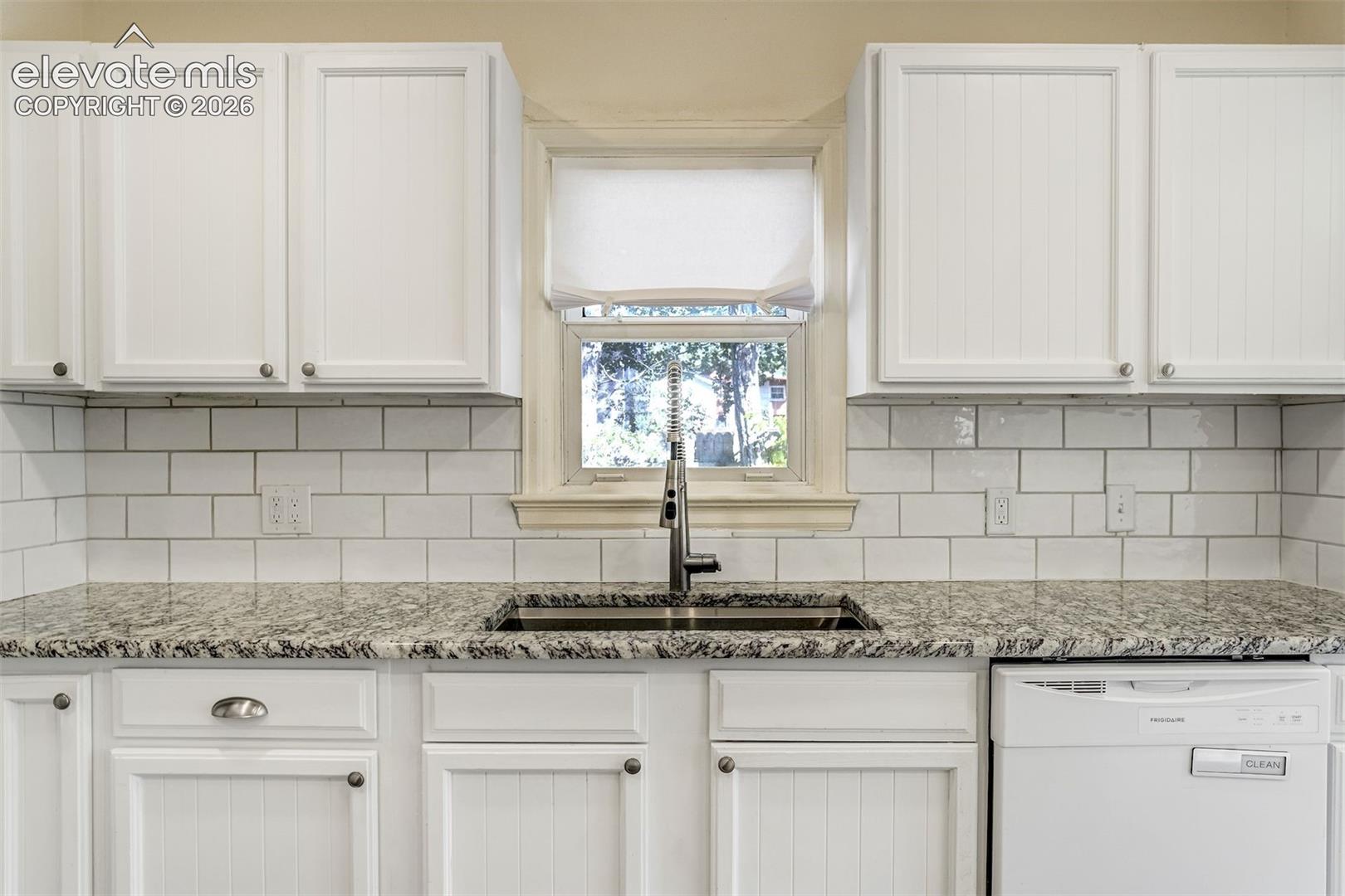 Kitchen featuring white beadboard cabinetry, stone-finish countertops, white subway tile backsplash, stainless steel under-mount sink with gooseneck faucet, and an integrated dishwasher