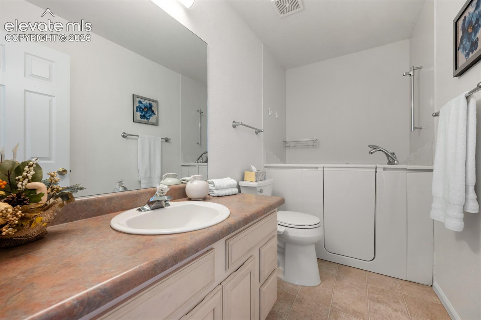 Bathroom featuring a vanity with an integrated oval sink and laminate countertop, a large wall-mounted mirror, and a walk-in tub with a handheld shower fixture