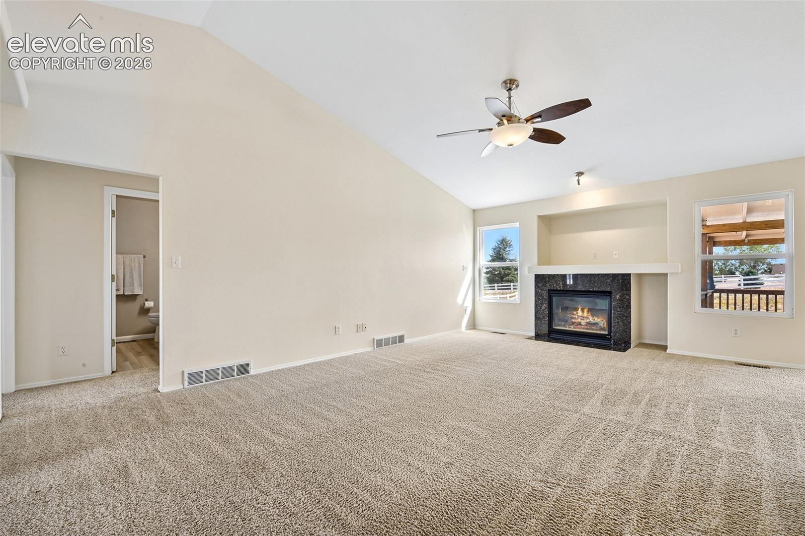 Vaulted ceiling with ceiling fan, recessed media niche with black stone-surround fireplace, and light carpet flooring
