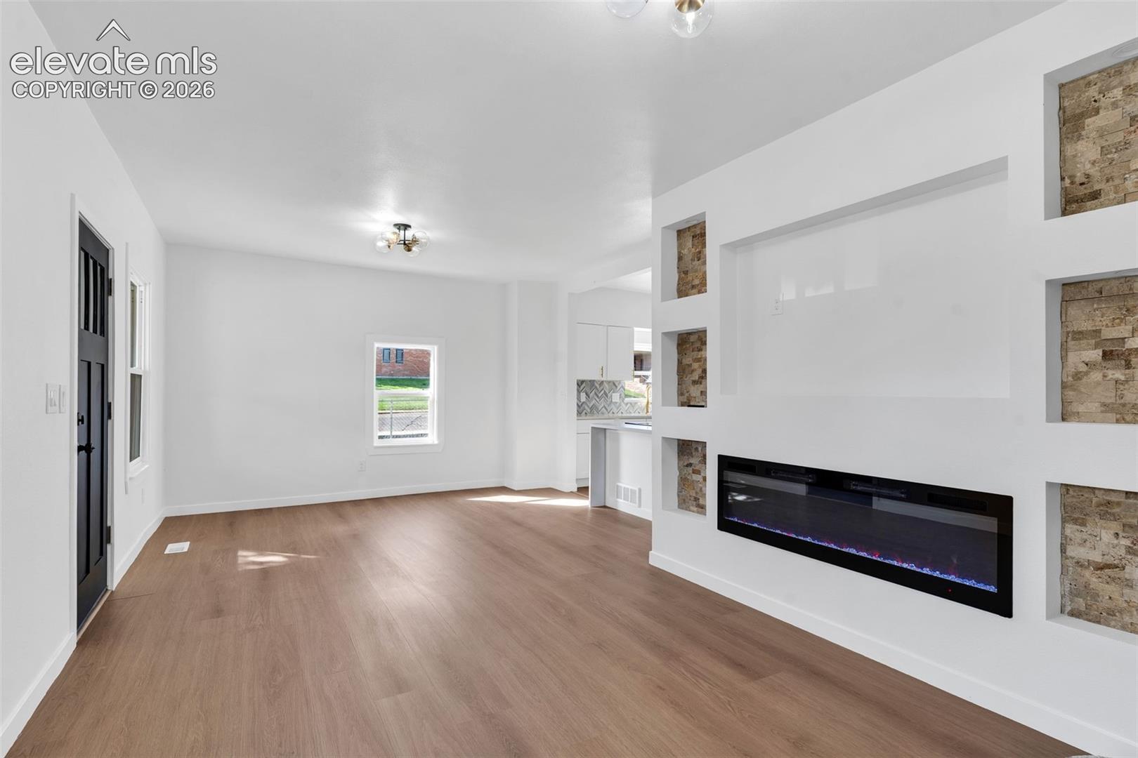 Living area featuring wood-finish flooring, a linear electric fireplace, custom recessed wall niches with stone-texture backing, and flush-mount ceiling light fixtures