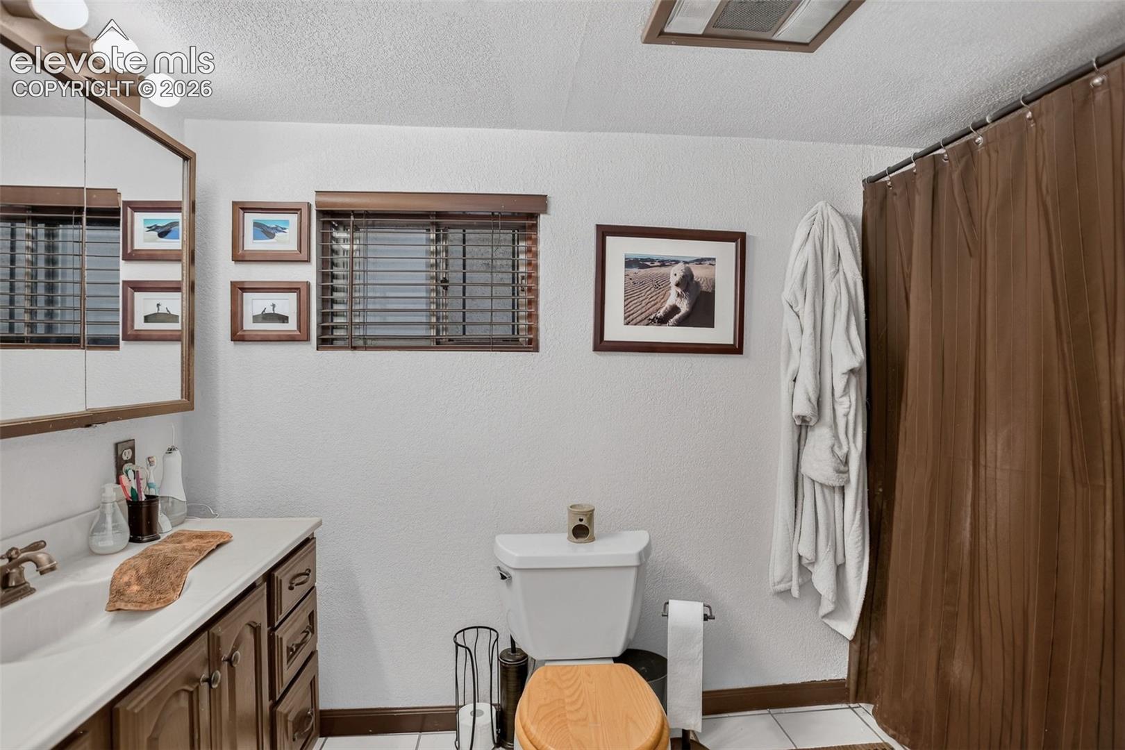 Bathroom featuring a vanity with a white countertop and wood-finish cabinetry, a wall-mounted medicine cabinet with integrated lighting, a toilet, and a shower/tub combination with a shower rod