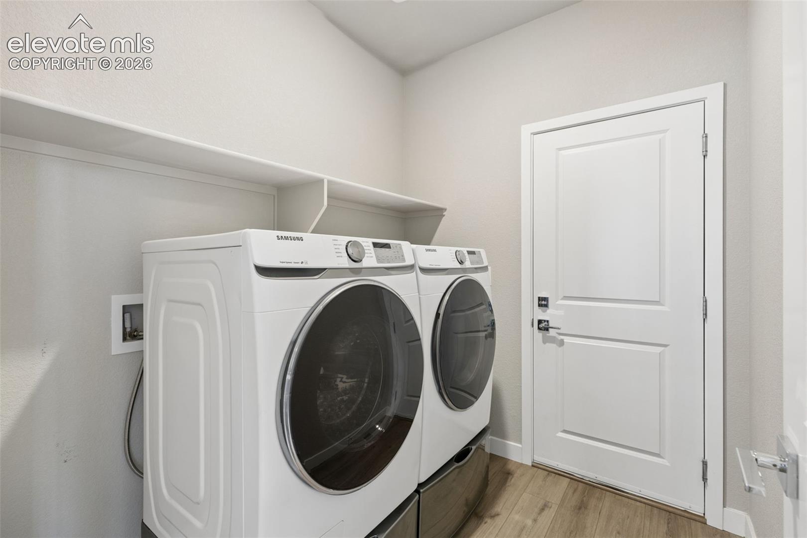 Utility room featuring wood-finish flooring, a white paneled door, and built-in overhead shelving