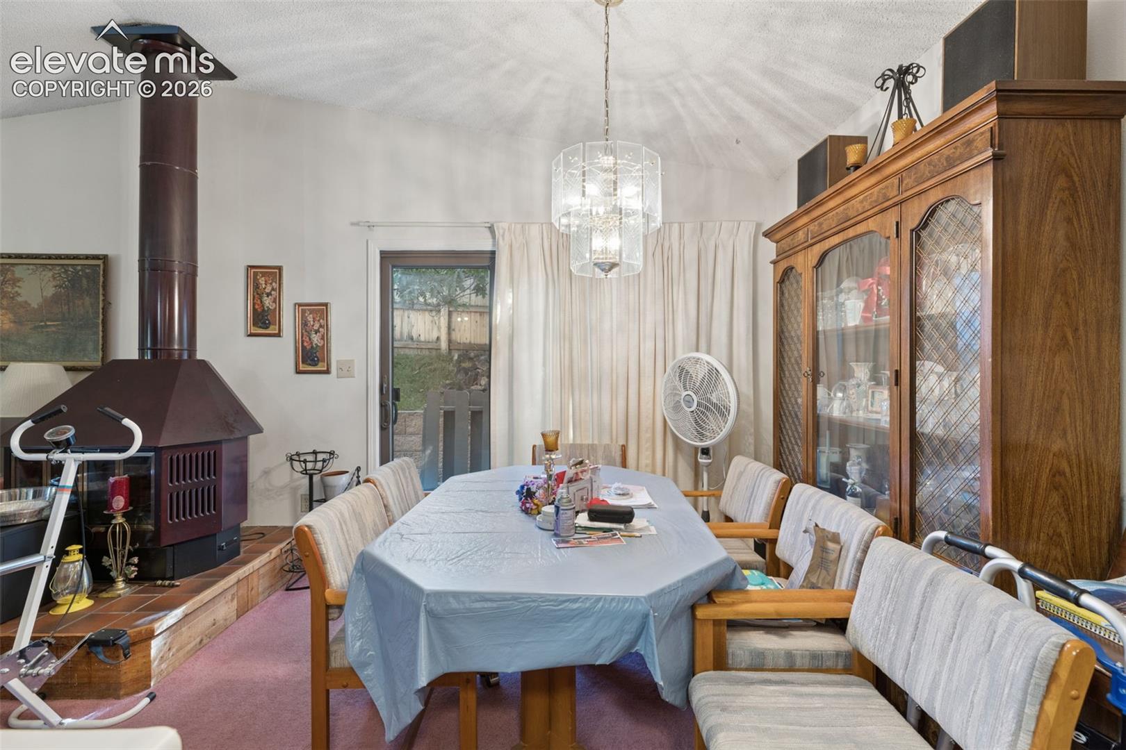 Vaulted ceiling, freestanding metal wood-burning stove on a raised tile hearth, and tiered crystal chandelier