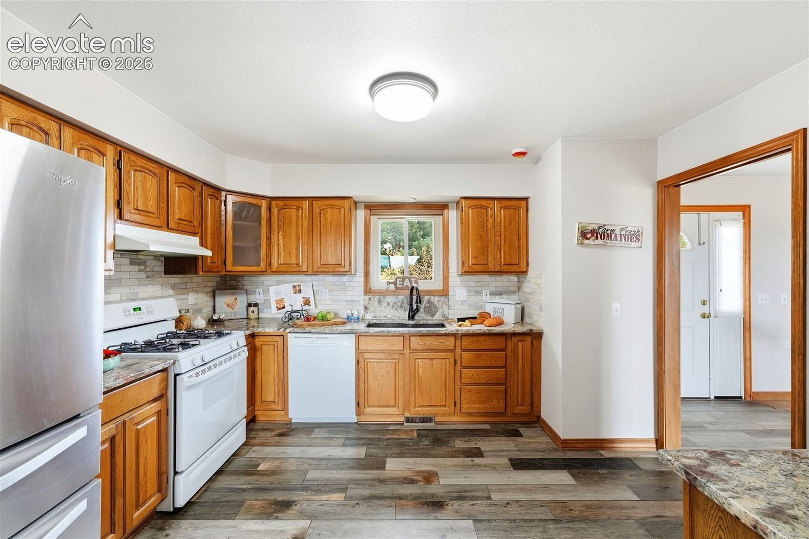 Kitchen featuring wood-finish flooring, wood cabinetry, granite-style countertops, and a subway tile backsplash