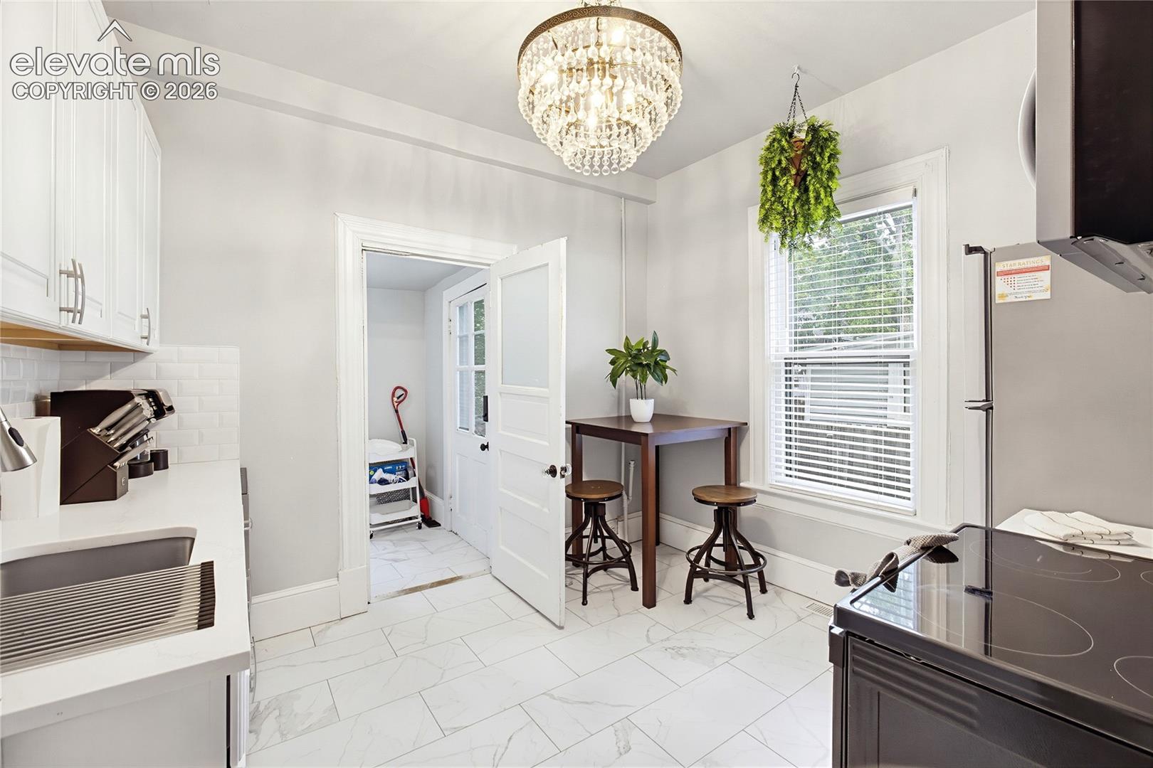 White shaker-style cabinetry with brushed nickel pulls, subway tile backsplash, under-mount sink, and a crystal-beaded chandelier