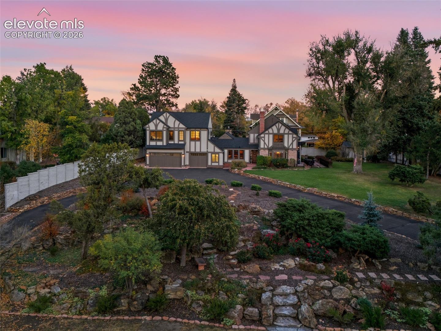 Tudor-style exterior featuring half-timbering, a multi-car garage, expansive rock garden landscaping, stone-paved pathways, and mature trees