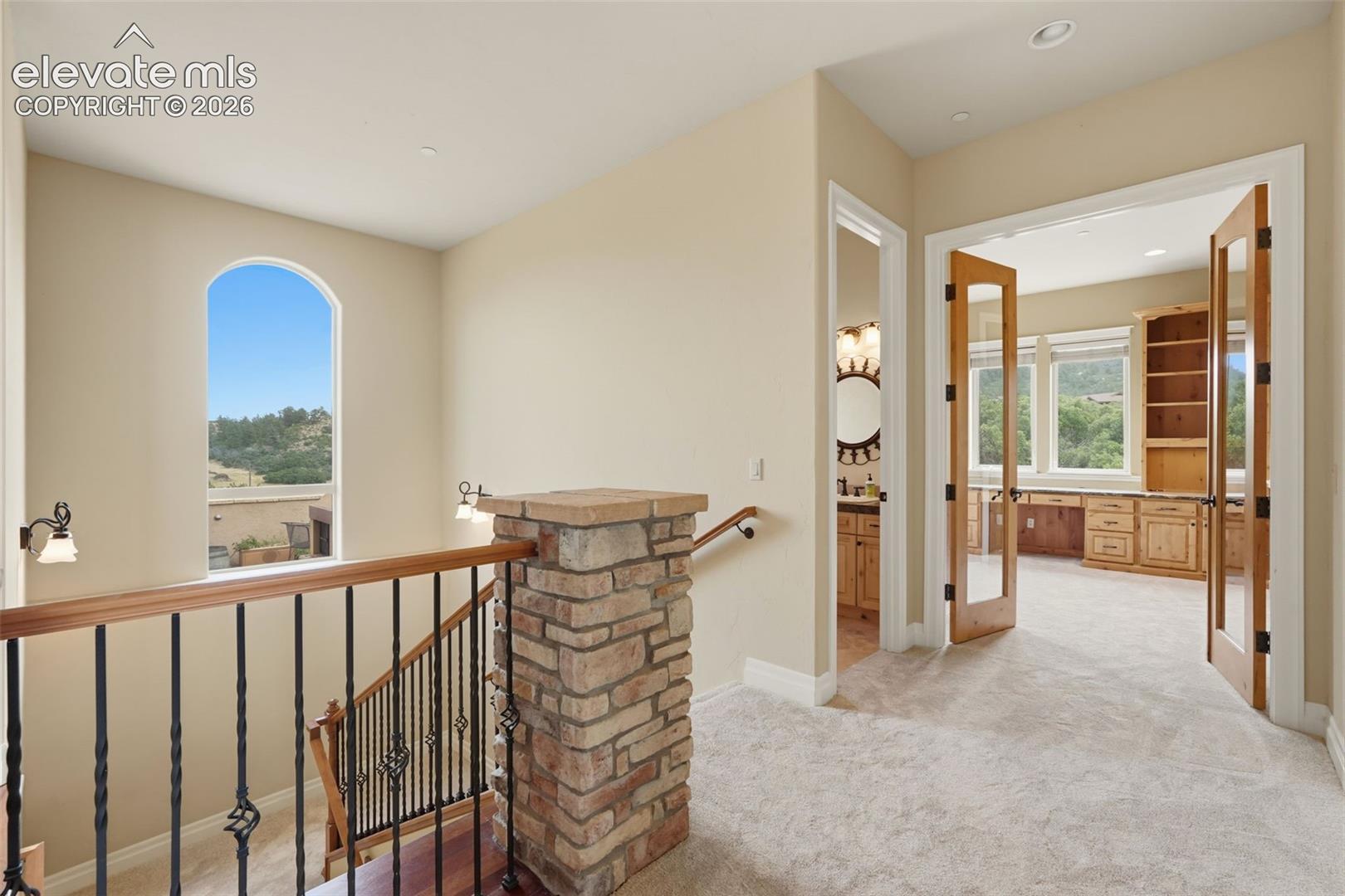 Upper-level landing featuring a stone pillar, wrought iron railing with wood-finish top, and an arched window