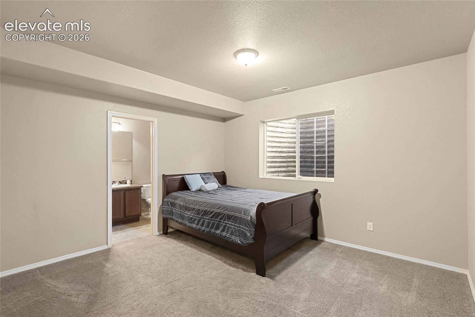 Neutral-toned interior room featuring wall-to-wall carpeting, recessed ceiling detailing, and a sliding window with an egress well