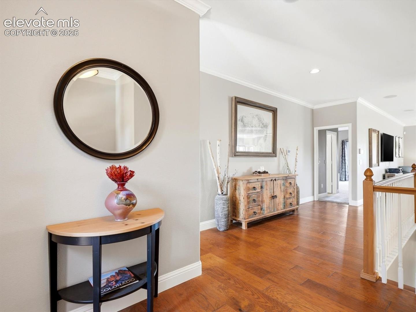 Hallway featuring wood-finish flooring, crown molding, and a staircase with a wooden handrail and balusters
