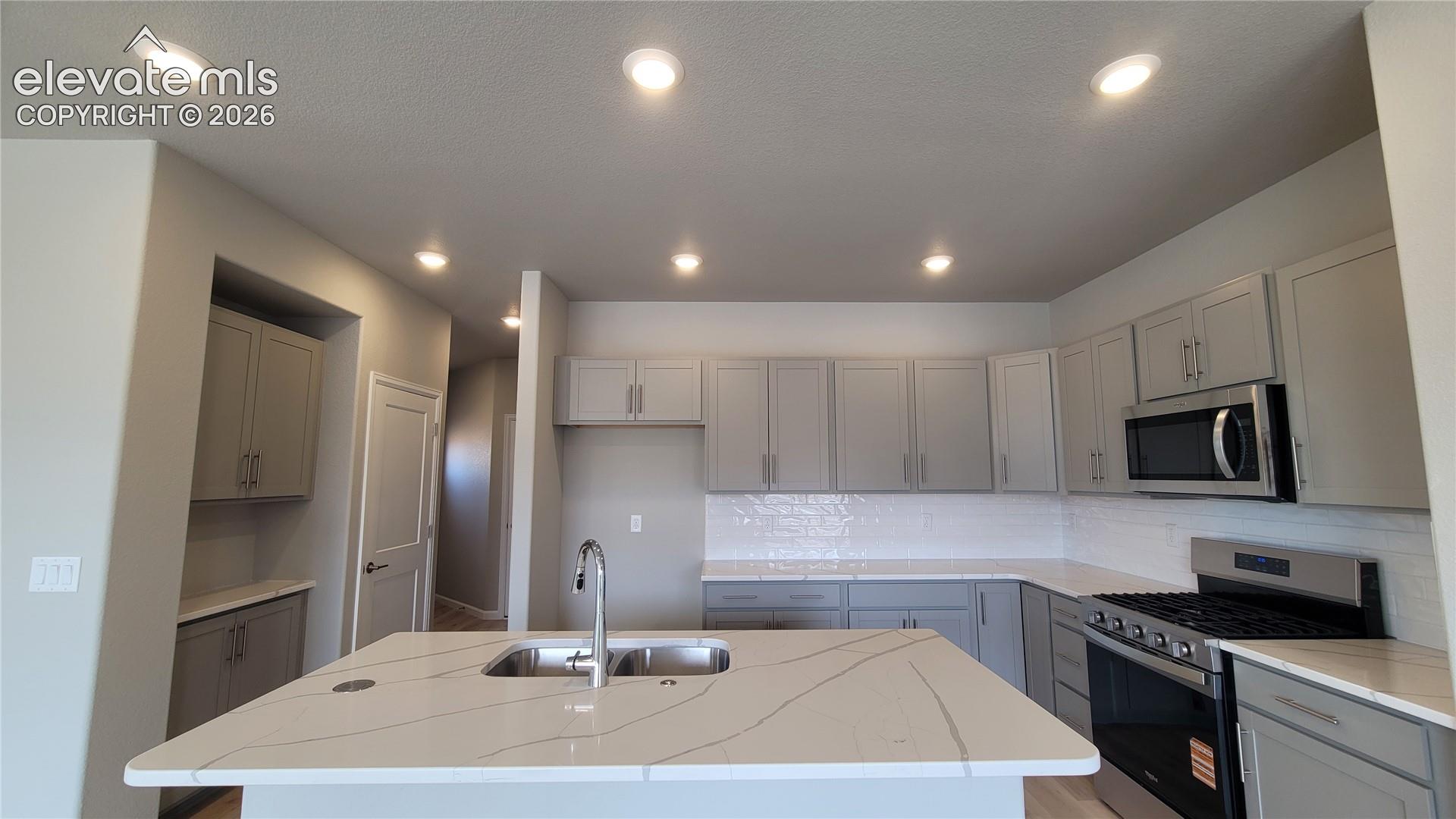 Kitchen with Quartz countertops, pantry, large island, and stainless steel gas range, microwave, and dishwasher! 
