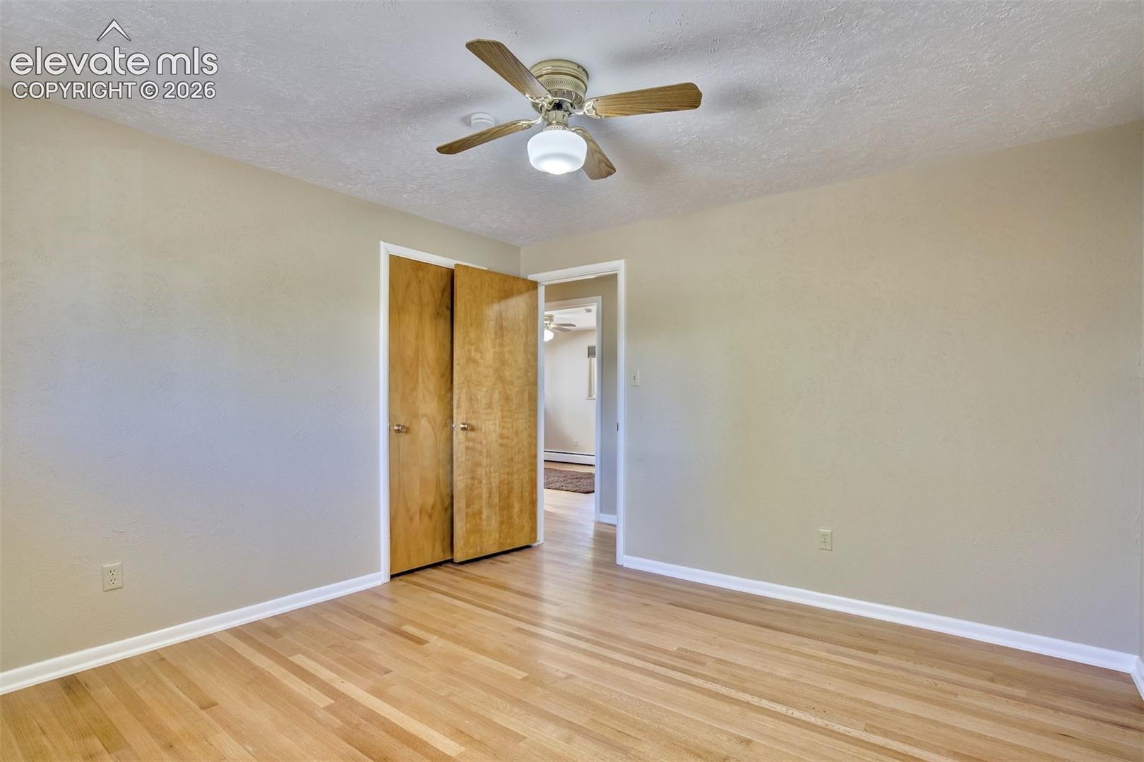 Room featuring wood-finish flooring, neutral wall paint, and a ceiling-mounted fan with integrated light fixture, finished with wood-panel swing-door closet