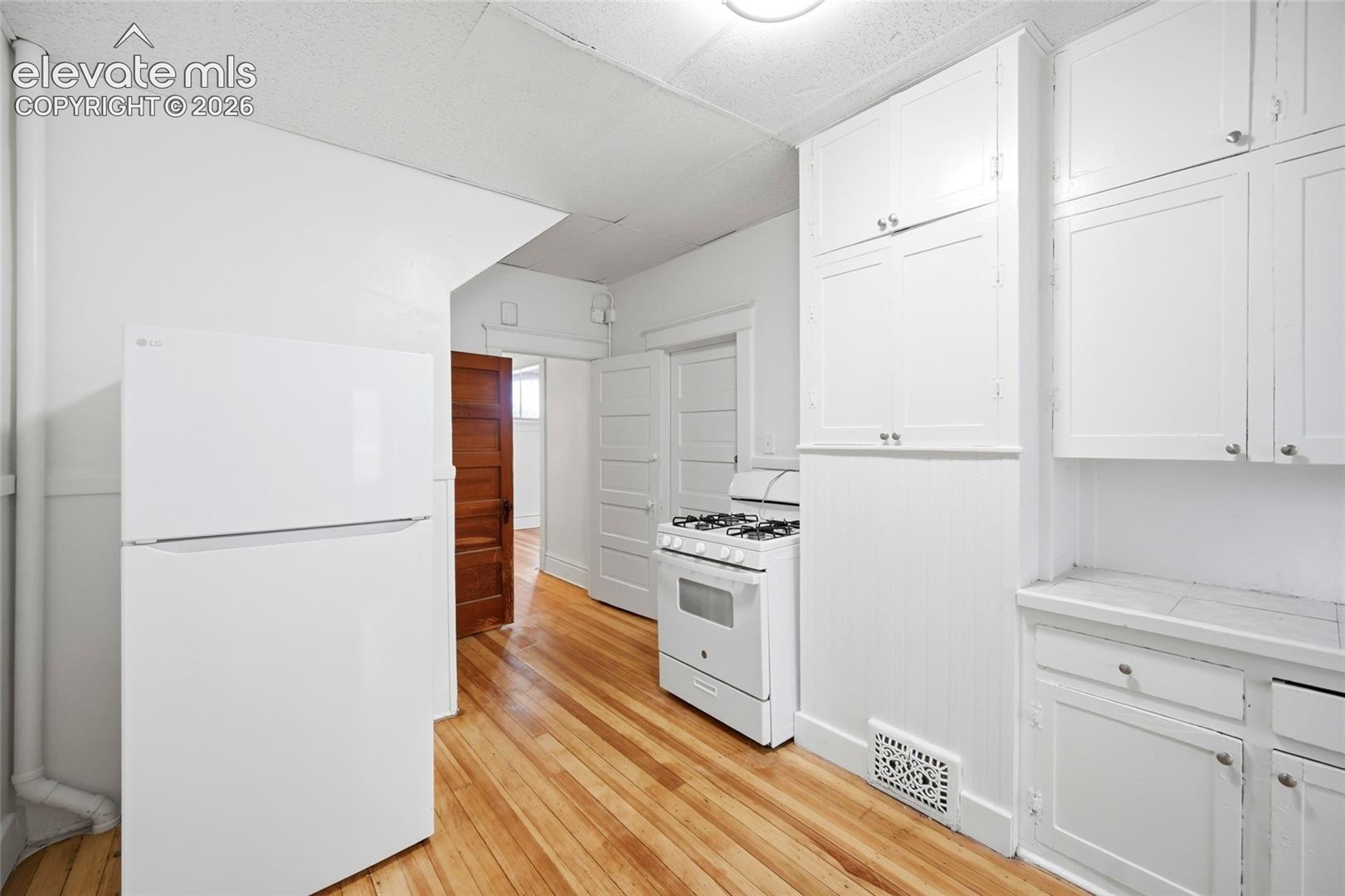 Kitchen featuring white cabinetry, wood-finish flooring, a white gas range, and a full-size refrigerator
