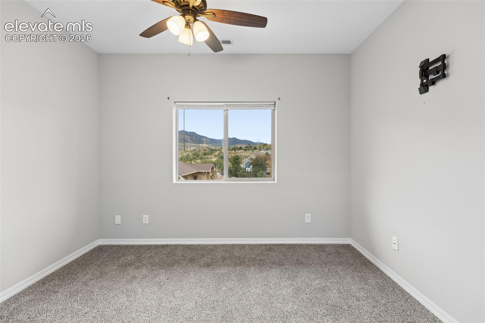 Neutral-toned interior space featuring wall-to-wall carpeting, a central ceiling fan with integrated lighting, and a single-pane window showcasing mountain scenery