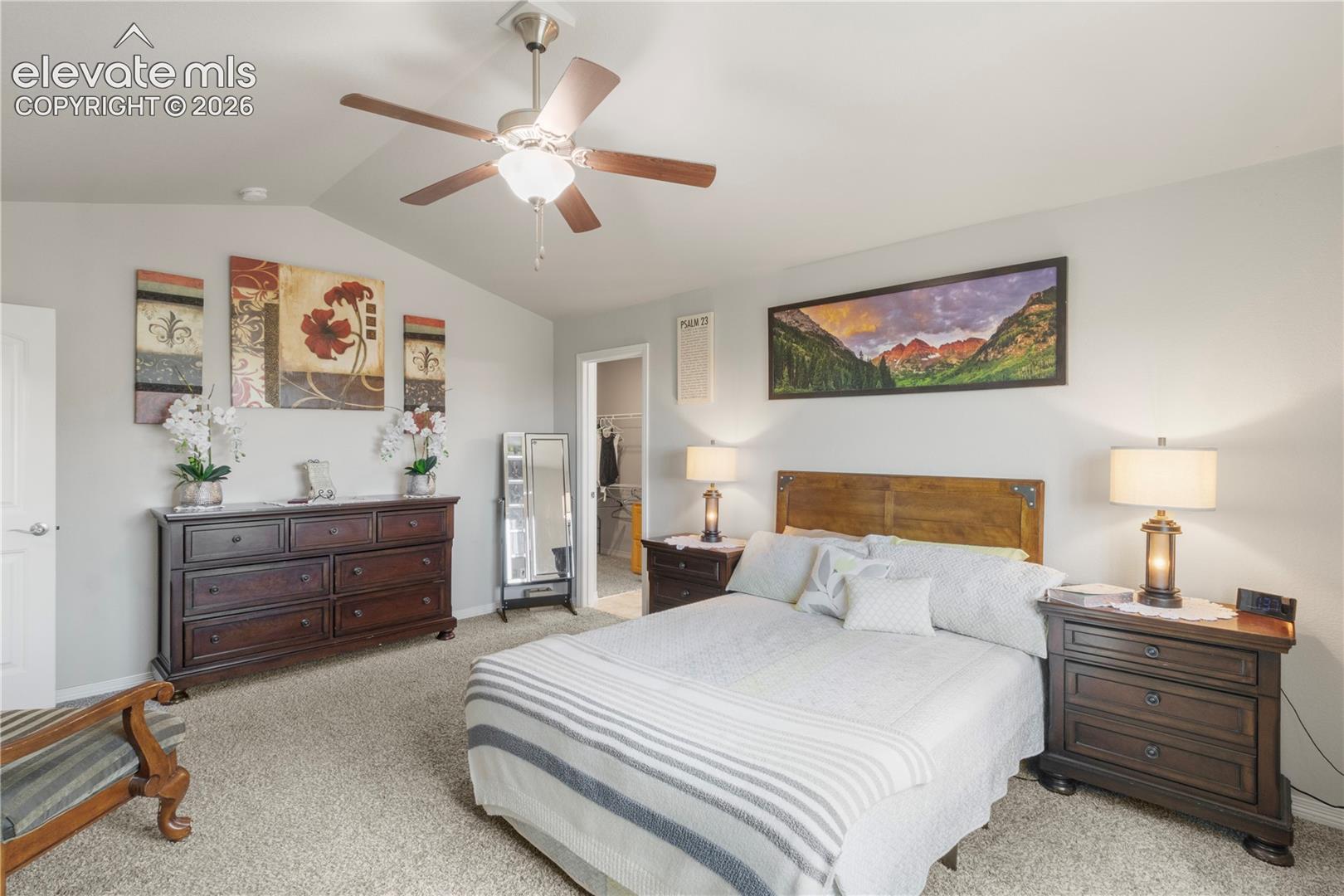 Vaulted ceiling, ceiling fan, carpet flooring, and a doorway leading to an additional space